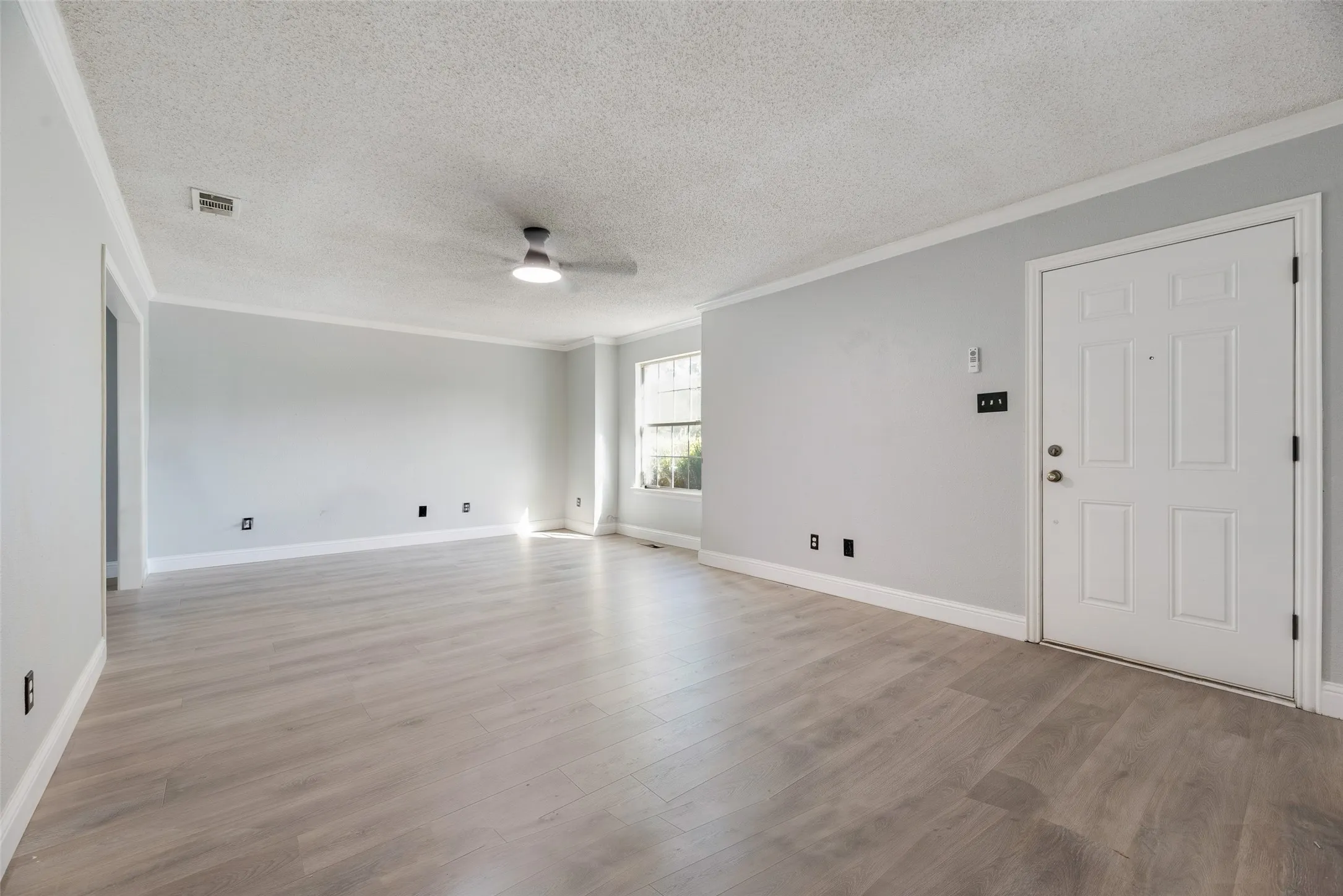 Spacious room with wood-finish flooring, light grey walls, white crown molding, and a modern ceiling fan