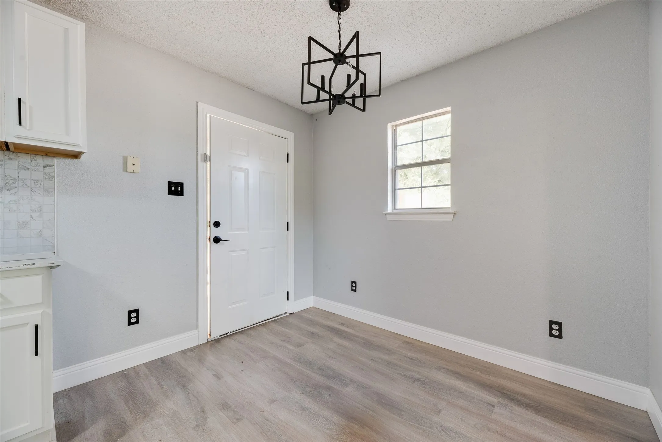 Light wood-finish flooring, white cabinetry, geometric ceiling light fixture, and a window with white trim
