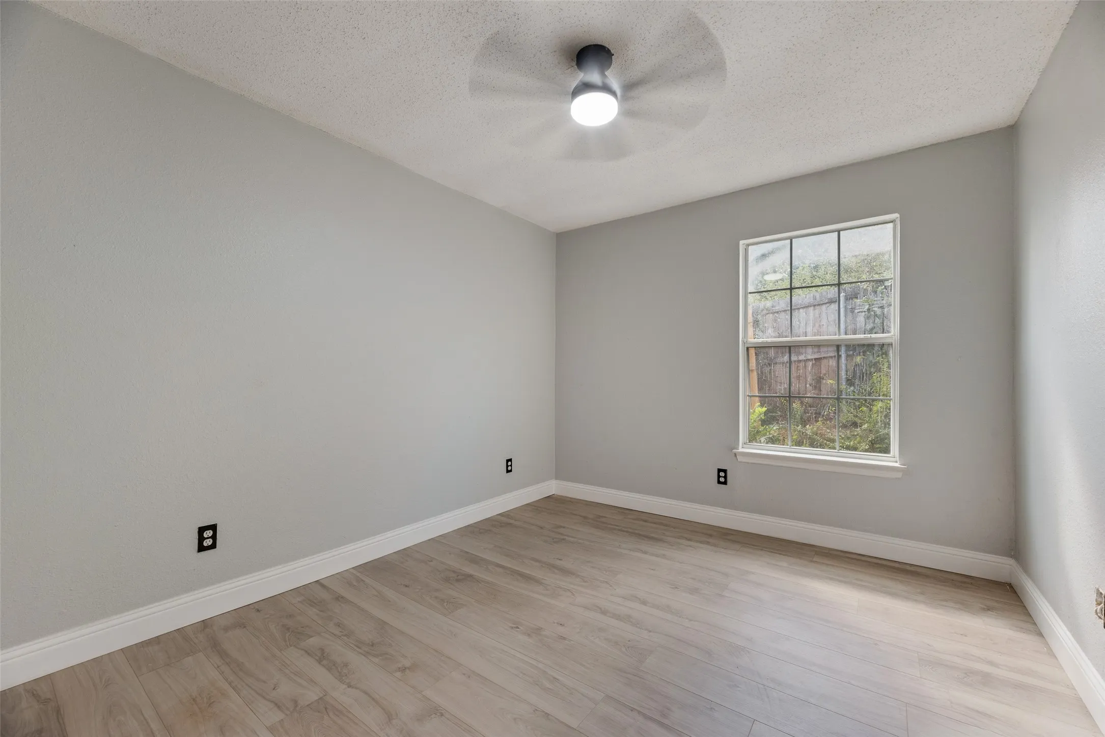 Neutral tone walls, wood-finish flooring, white window trim, and a ceiling fan with integrated lighting