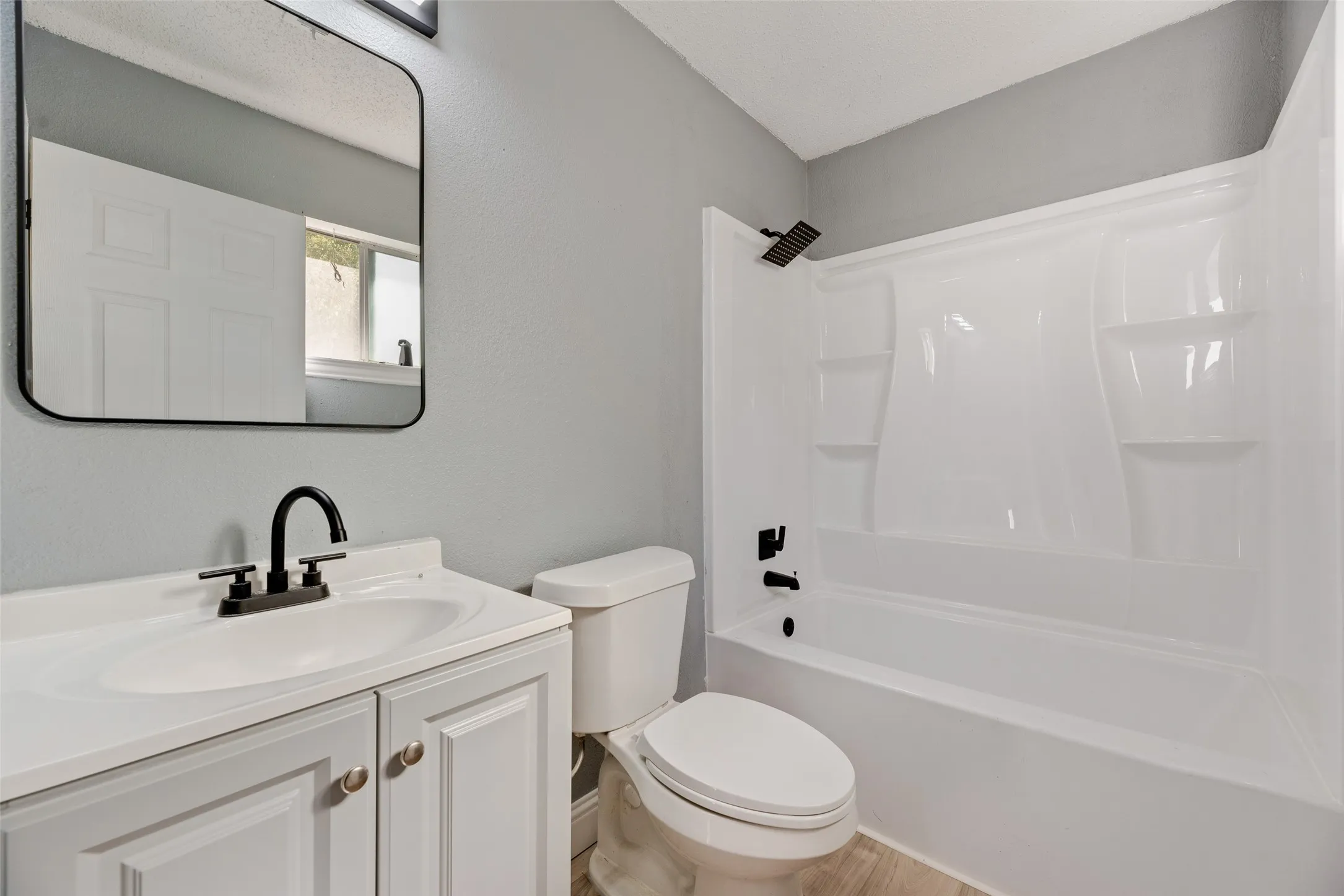 Bathroom featuring a white vanity with integrated sink, black fixtures, and a white tub/shower combination with built-in shelving