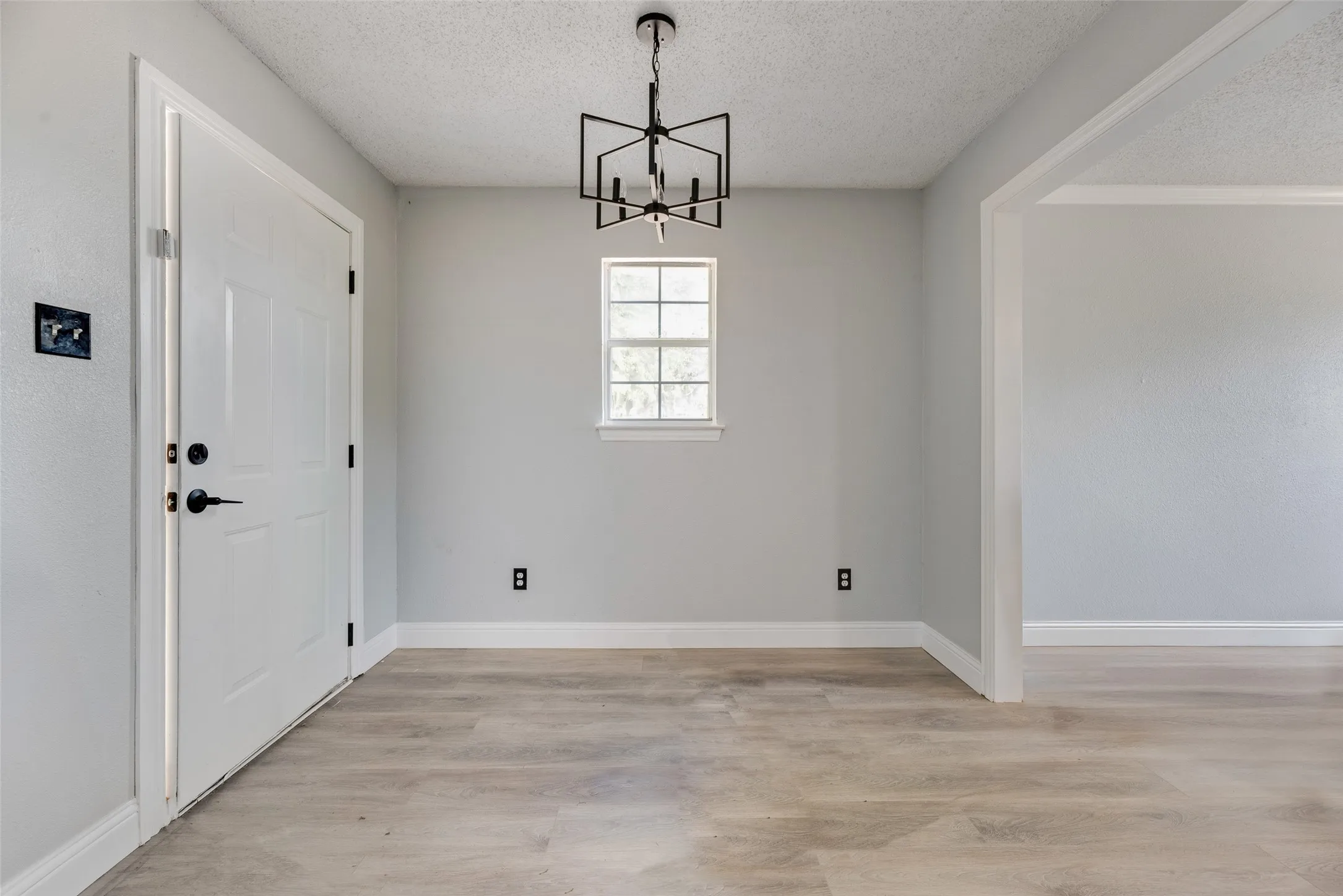 Wood-finish flooring, contemporary chandelier, white trim, and a window for natural light