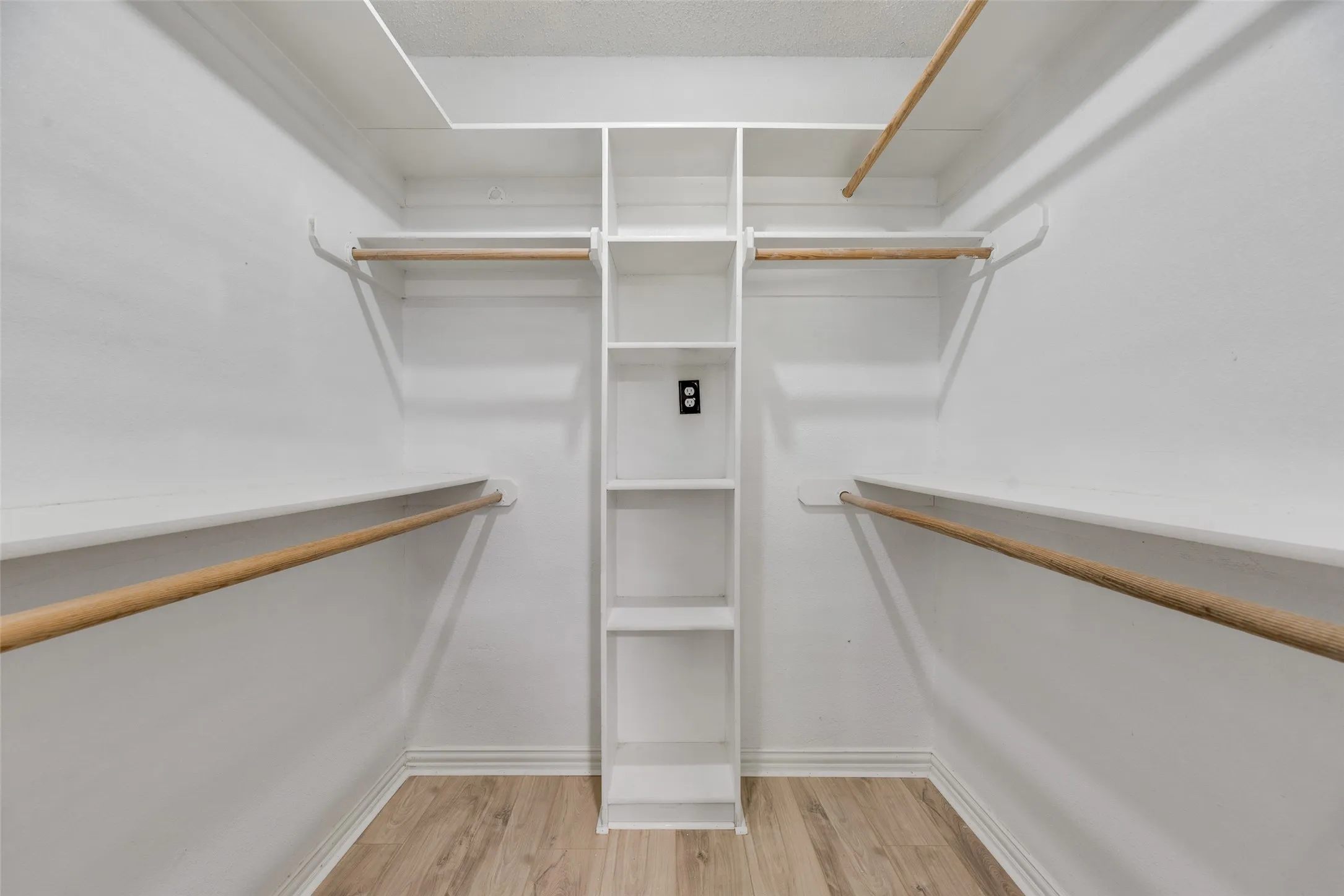 White built-in shelving, multiple hanging rods, and wood-finish flooring