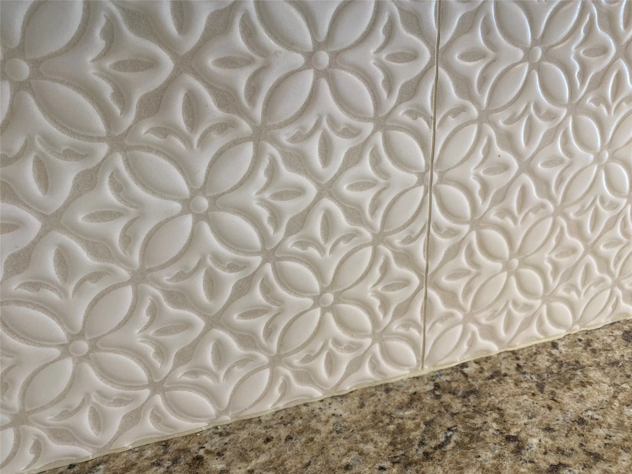 Embossed tile backsplash with a floral pattern, complementing a speckled countertop