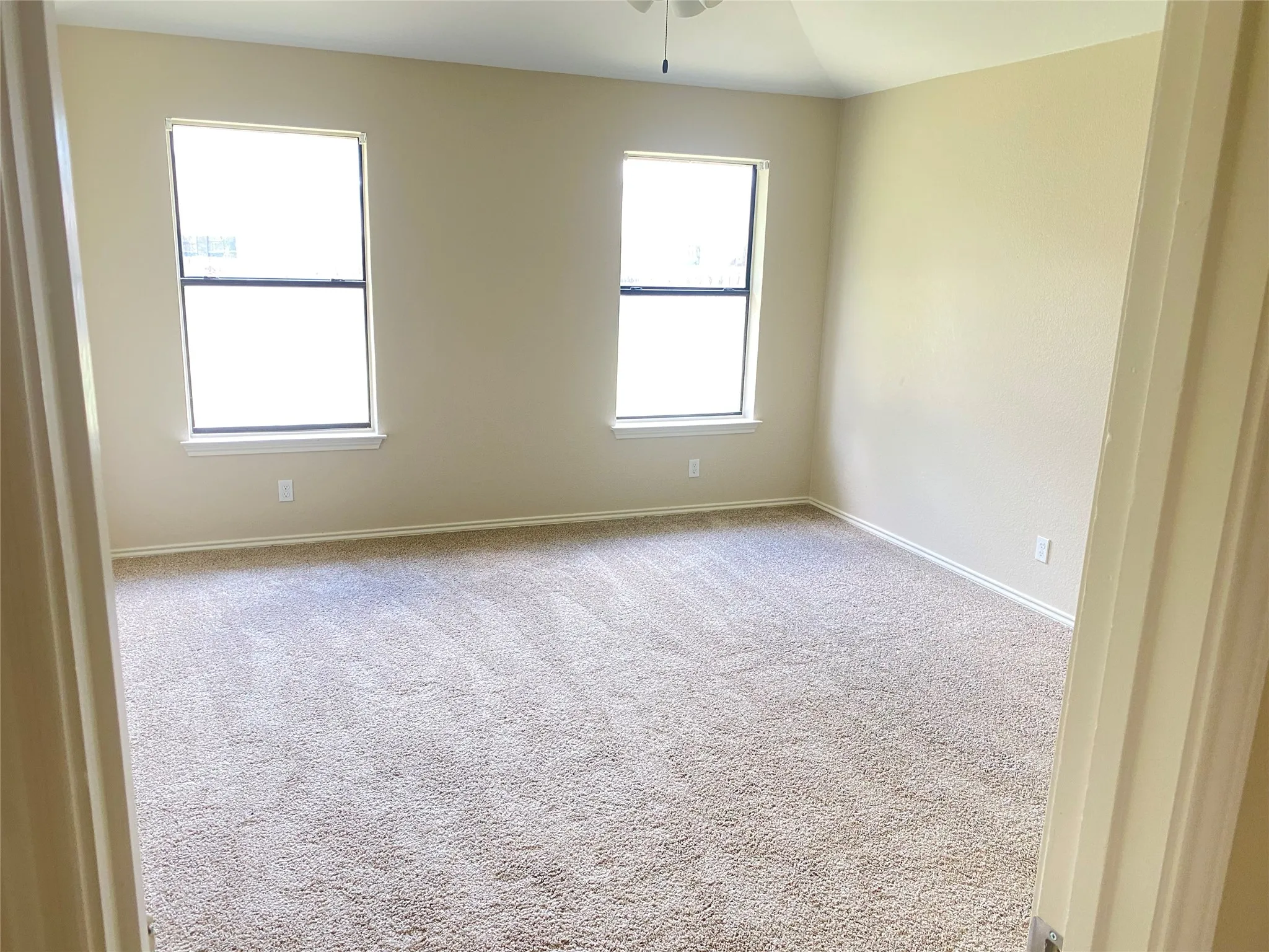 Neutral tone wall color, two windows with white trim, tan carpeting, and a ceiling fan