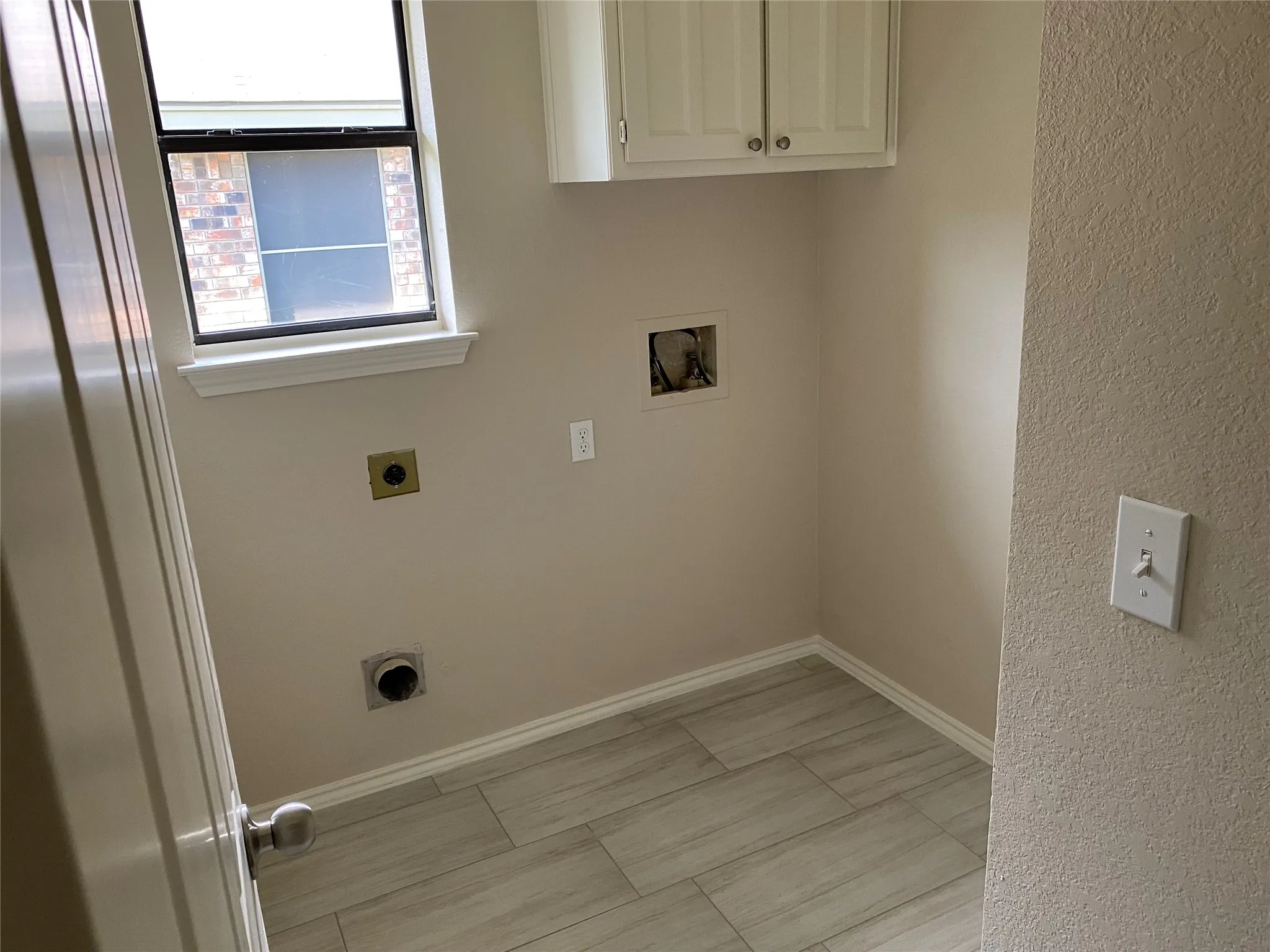 Utility space with wood-finish tile flooring, a single window, and upper cabinetry