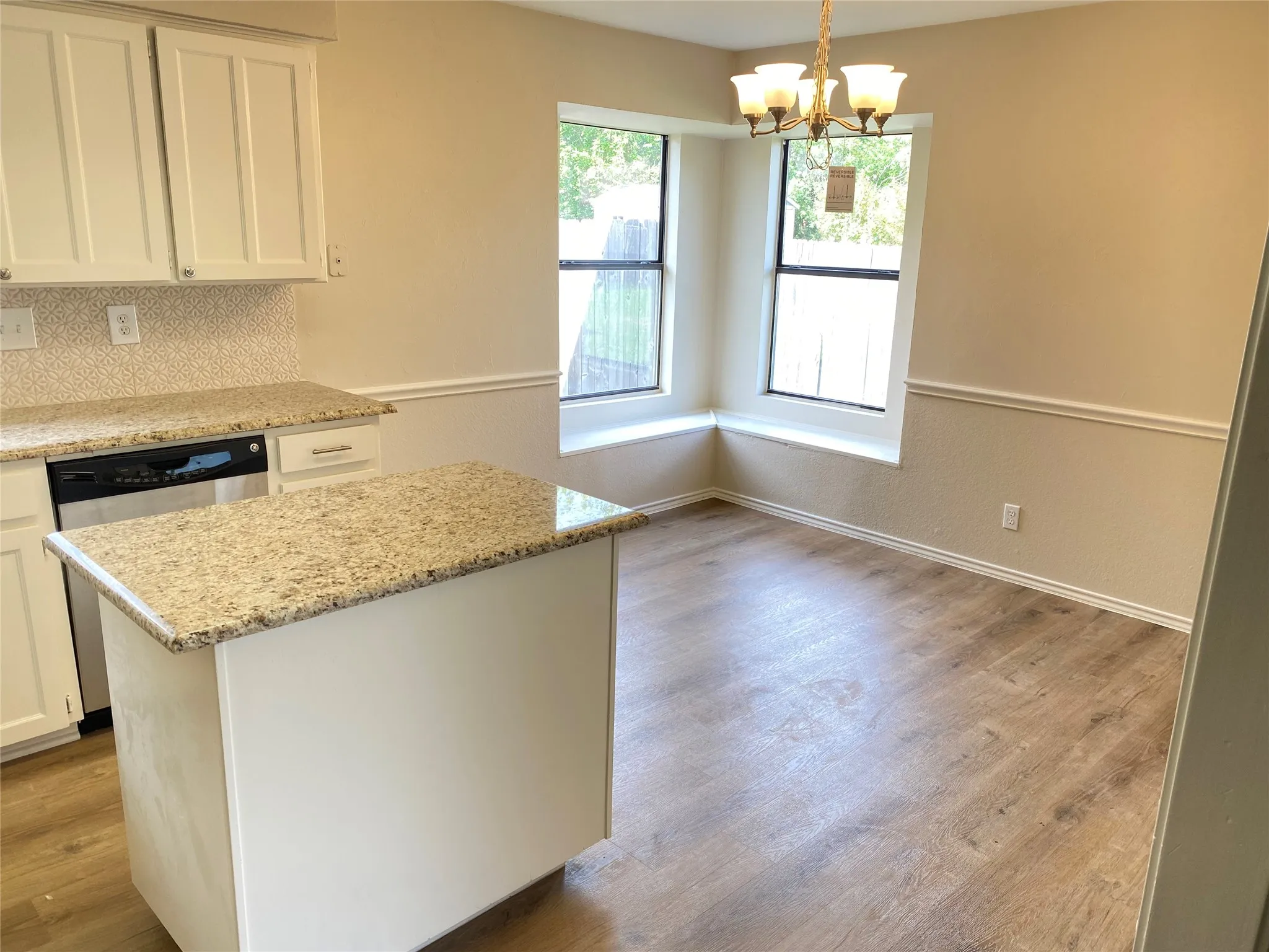 Kitchen featuring white cabinetry, a built-in stainless steel dishwasher, and an island with a stone-finish countertop