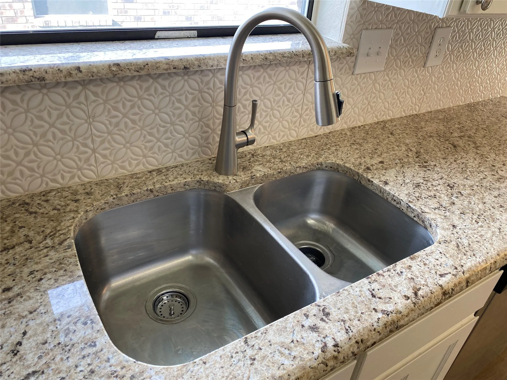 Dual basin stainless steel sink with a brushed nickel pull-down faucet, set into a granite countertop, complemented by a patterned tile backsplash