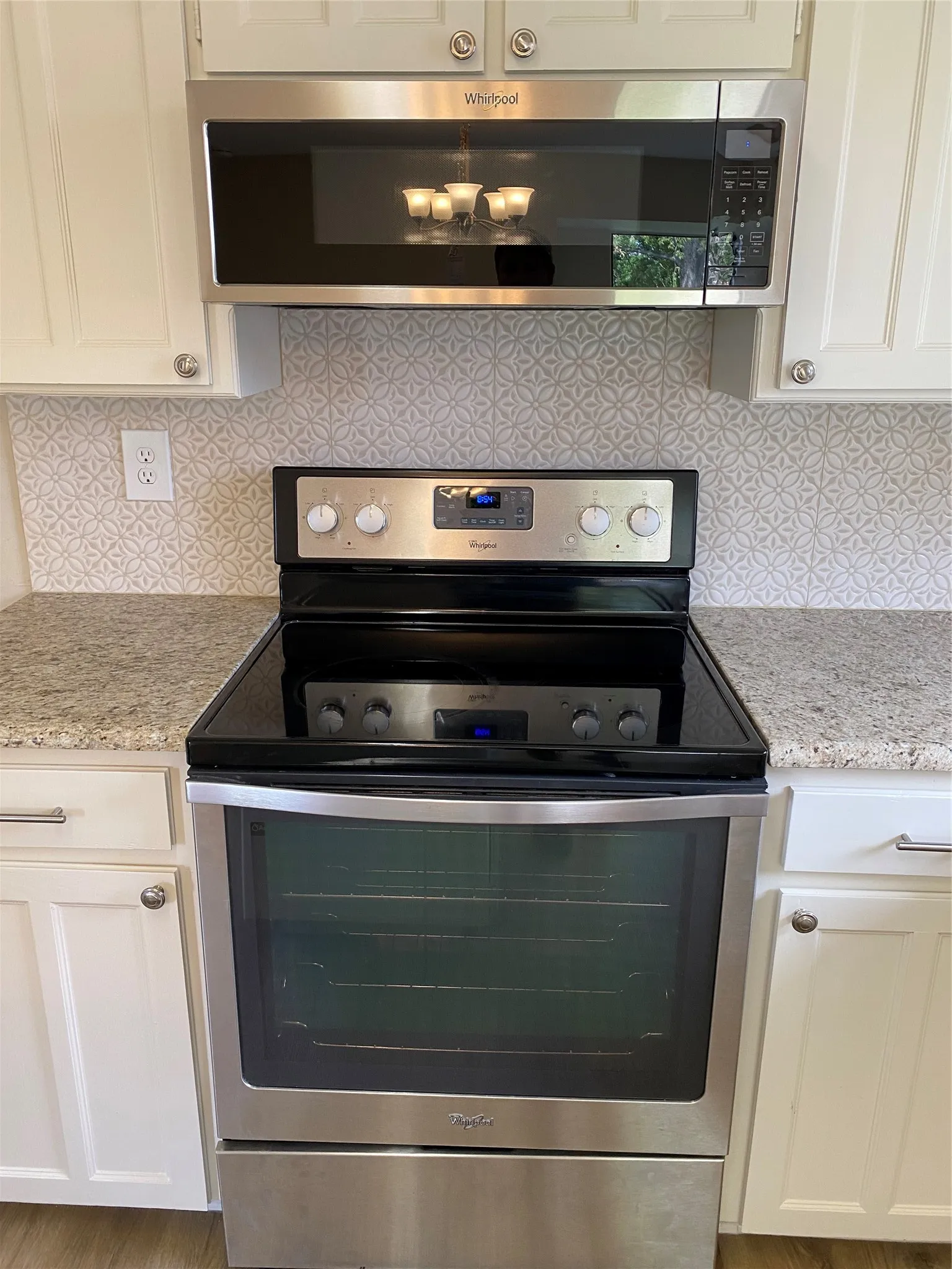 Stainless steel range, coordinating stainless steel microwave, white shaker-style cabinetry, patterned tile backsplash, and granite countertops