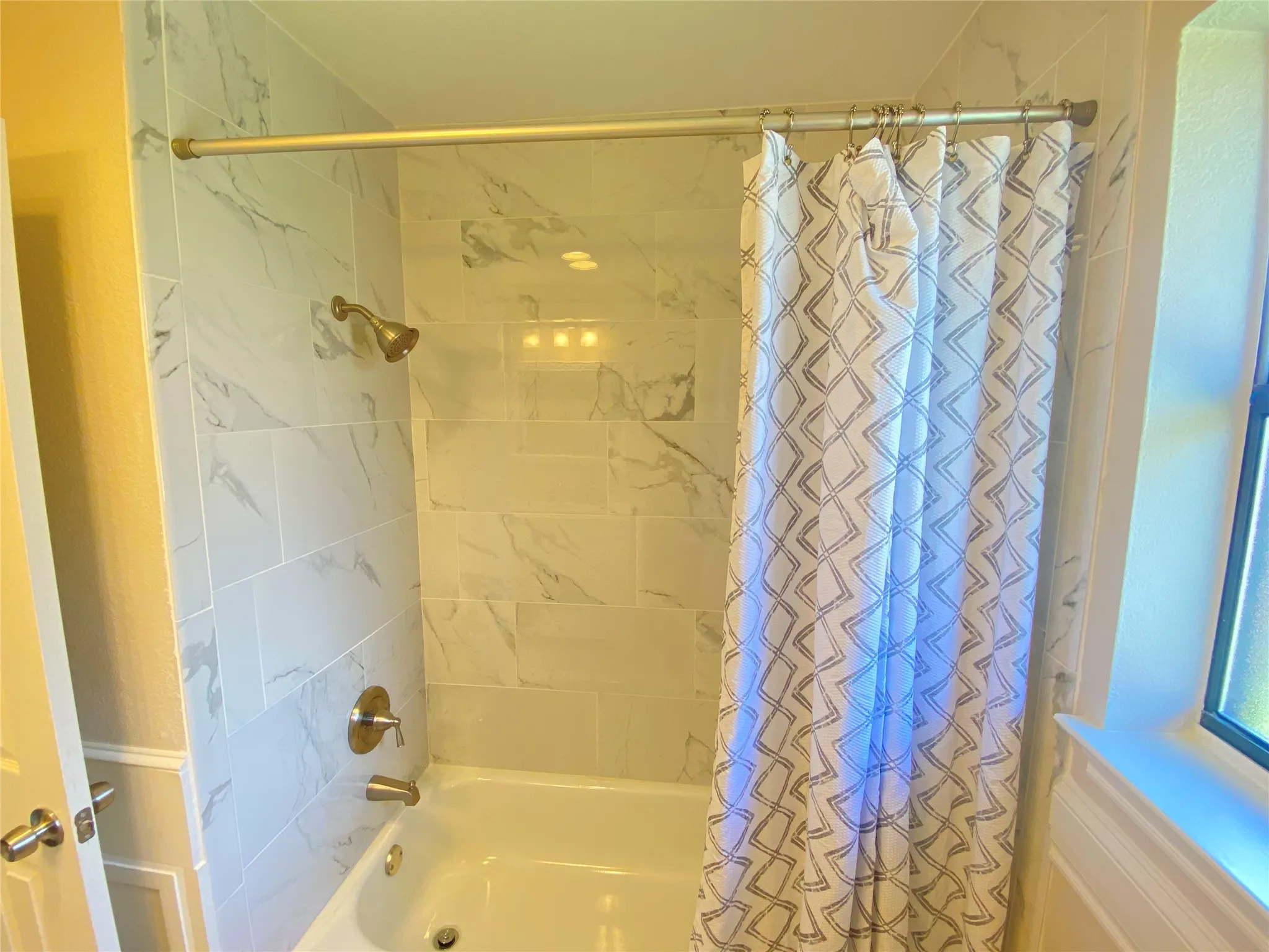 Bathtub with white subway tile surround, brass-finish shower fixtures, and integrated overhead lighting