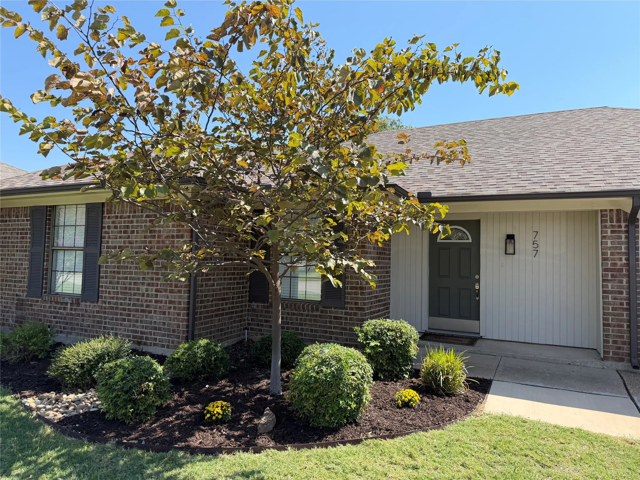 Brick exterior with vertical siding accents, dark entry door with arched transom, and a well-maintained front landscaping with mature shrubs