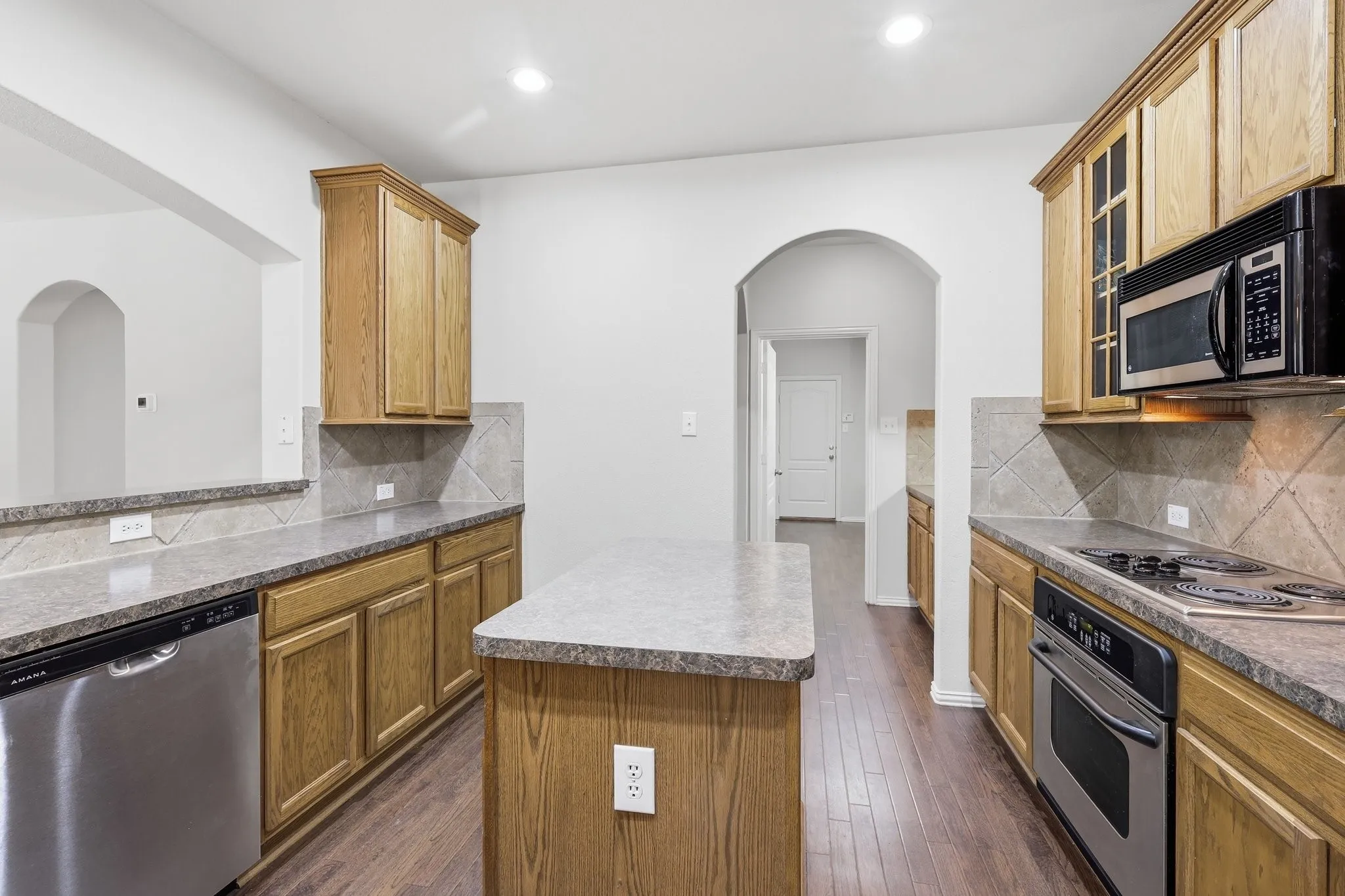 Kitchen featuring wood-finish flooring, wood cabinetry, stone-finish countertops, stainless steel dishwasher, and a built-in microwave