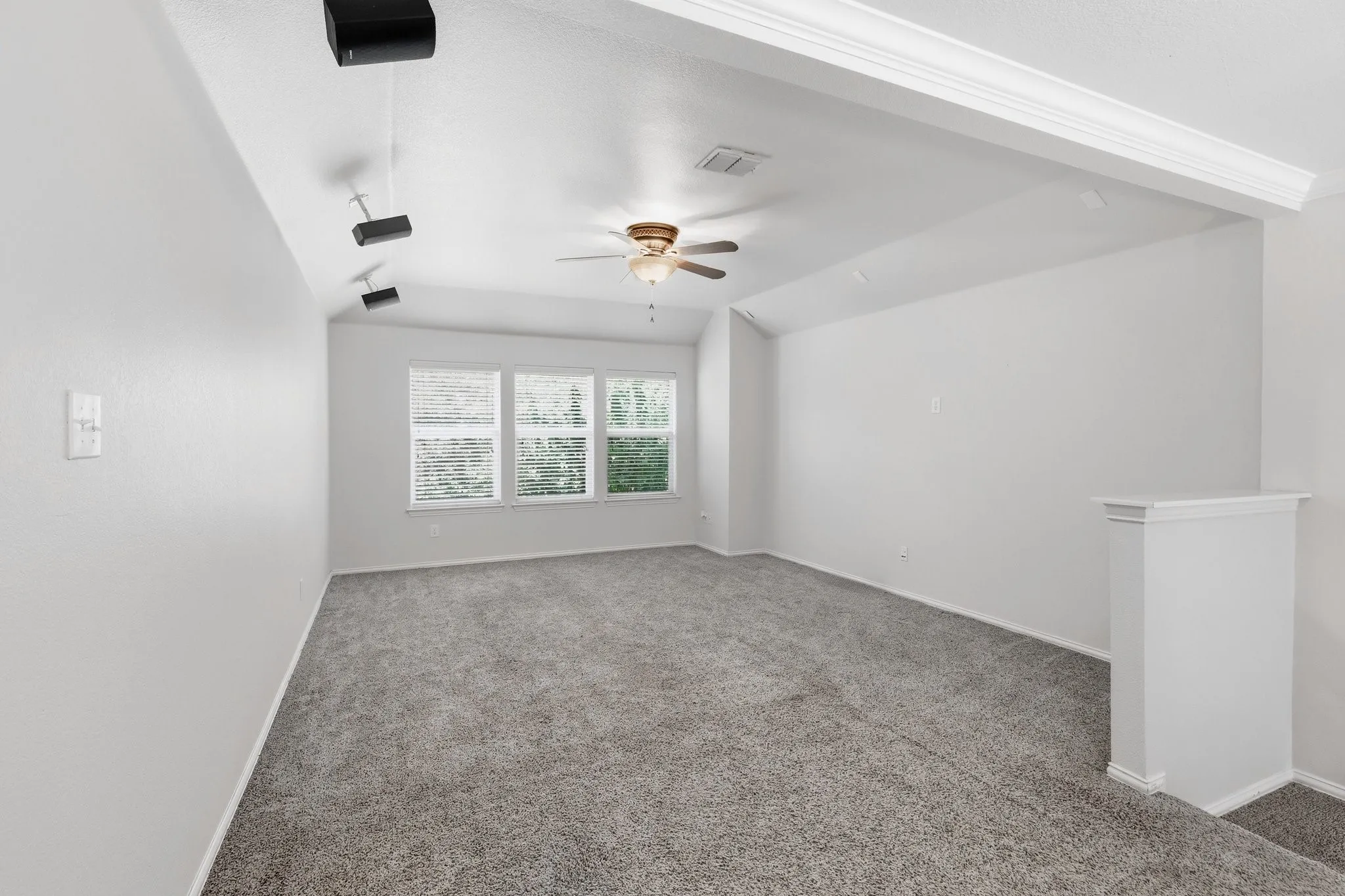Three windows with blinds, ceiling fan, vaulted ceiling, and carpeted flooring