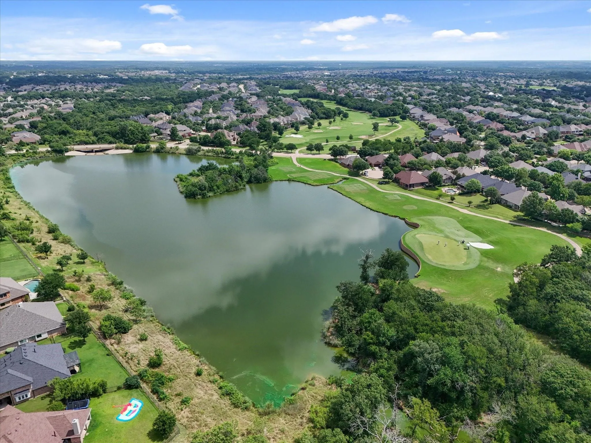 Expansive aerial showcasing a residential community, a substantial body of water, a golf course with greens, and mature landscaping