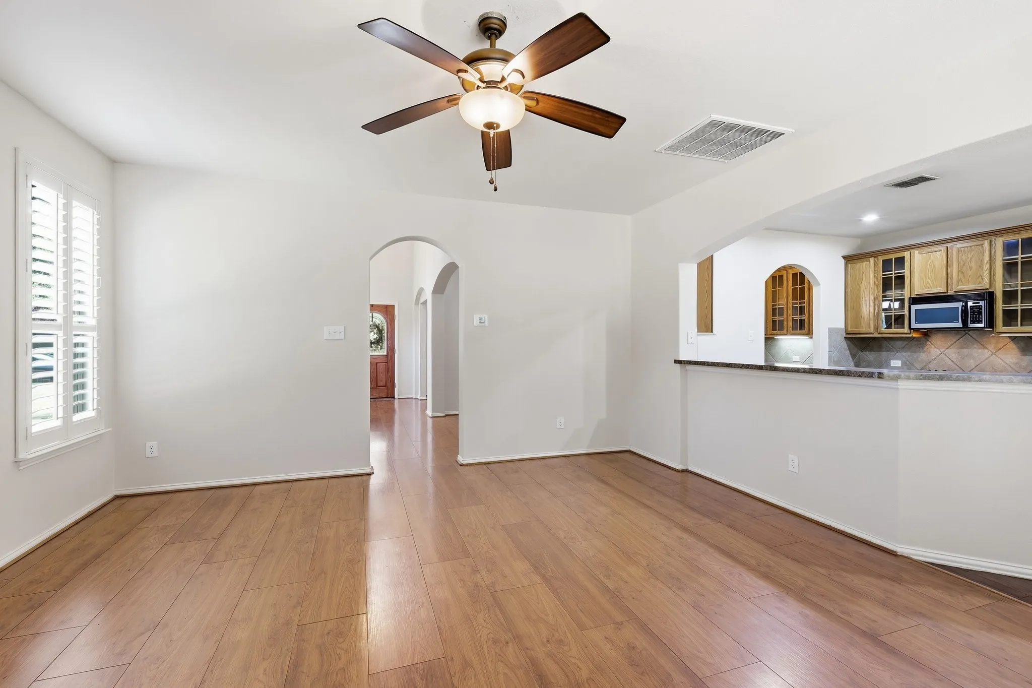 Wood-finish flooring, plantation shutters, arched doorways, ceiling fan, and a kitchen pass-through with a breakfast bar