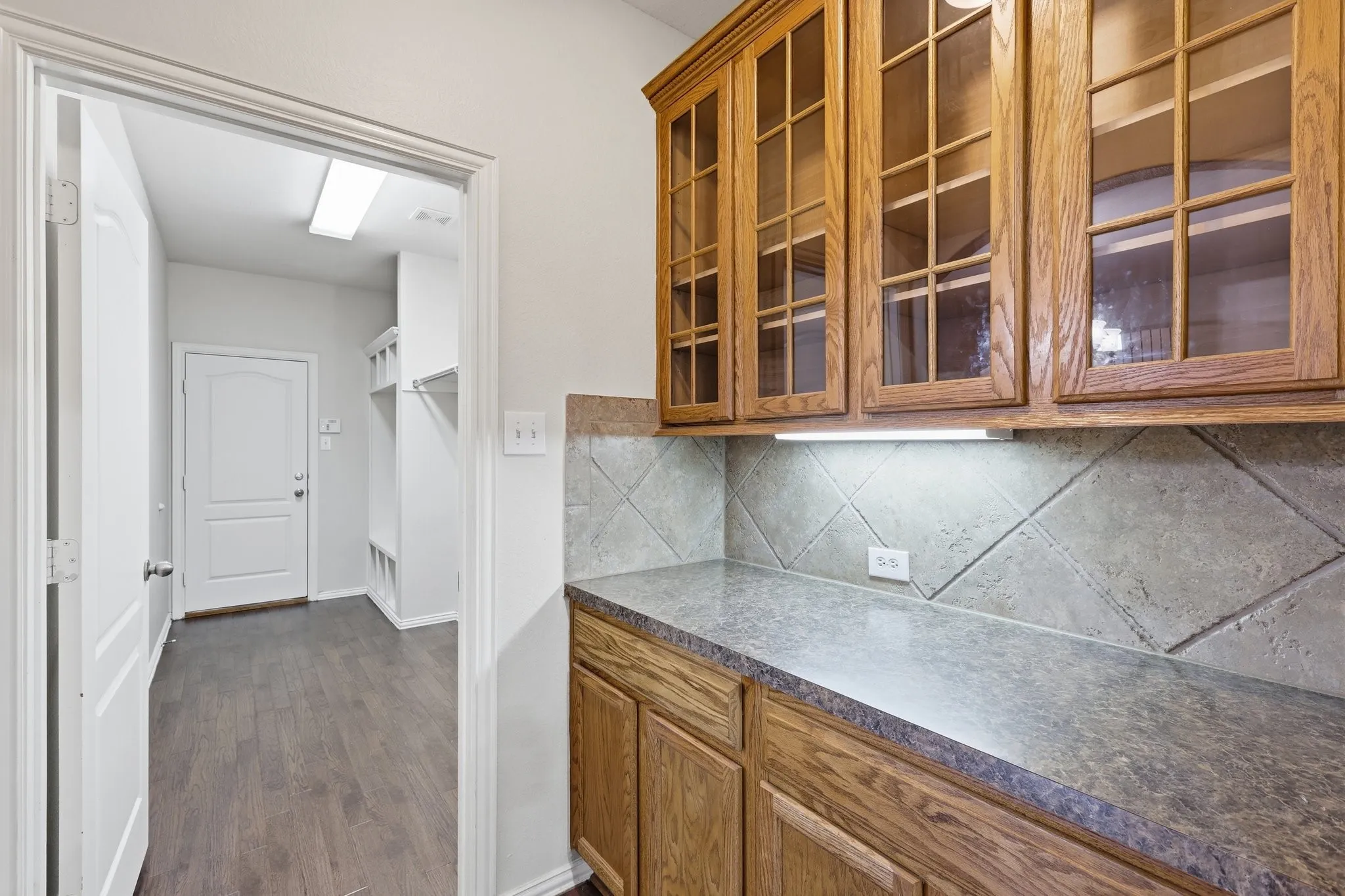 Wood-finish cabinetry with glass upper doors, under-cabinet lighting, and a durable countertop