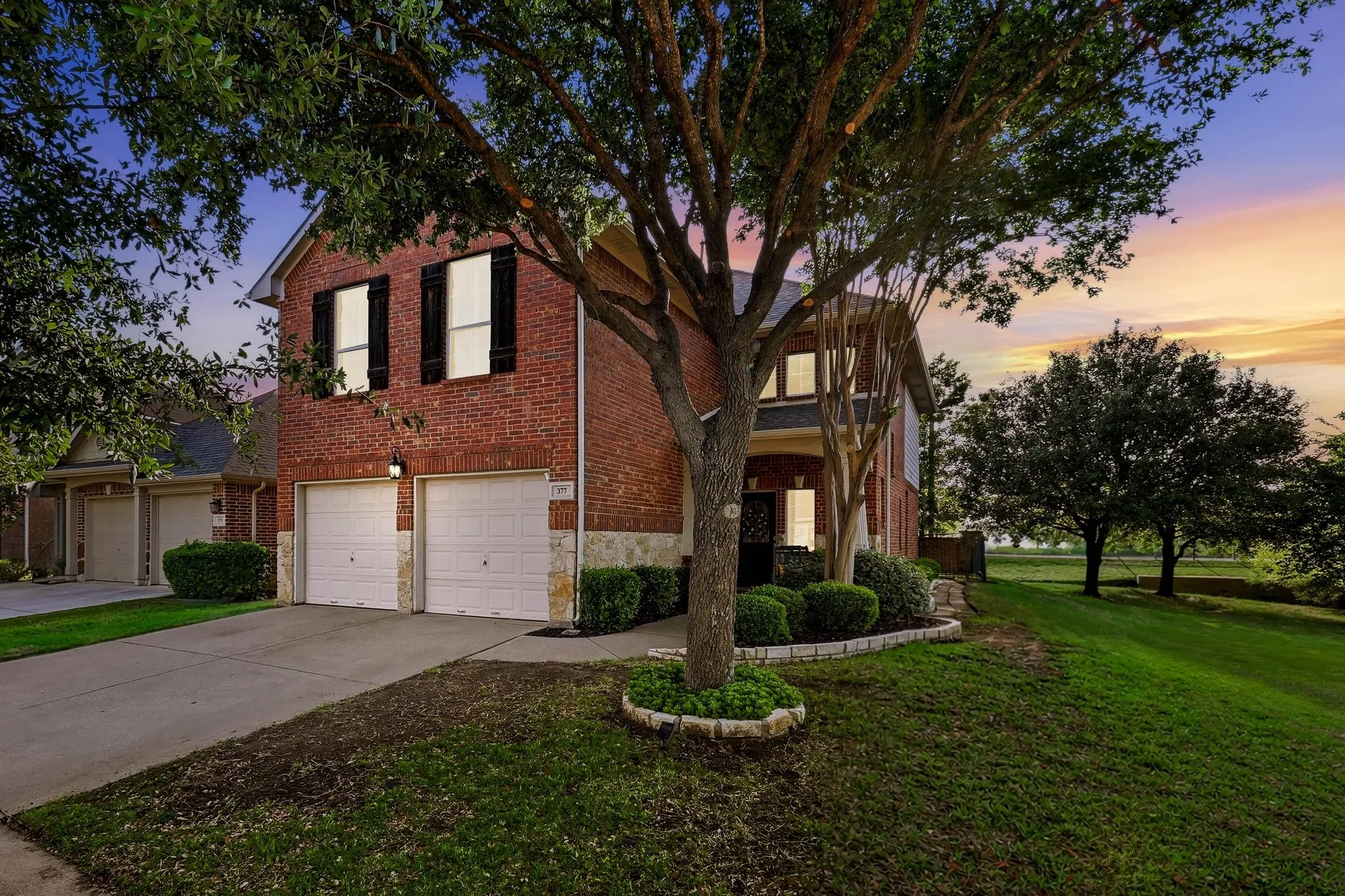 Brick exterior with stone accents, mature trees, and a two-car garage