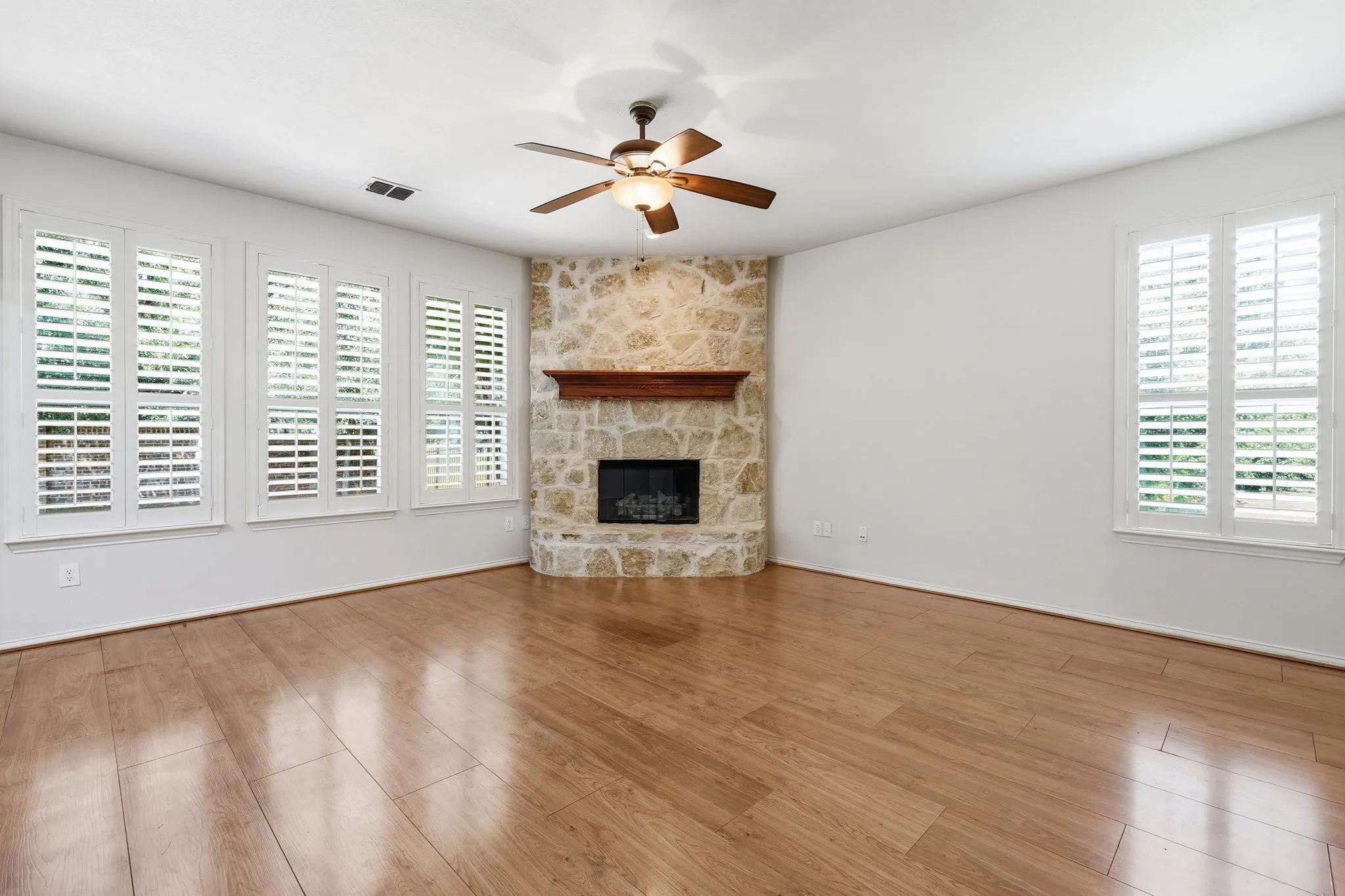 Stone-clad fireplace with a wood mantle, wood-finish flooring, and white plantation shutters