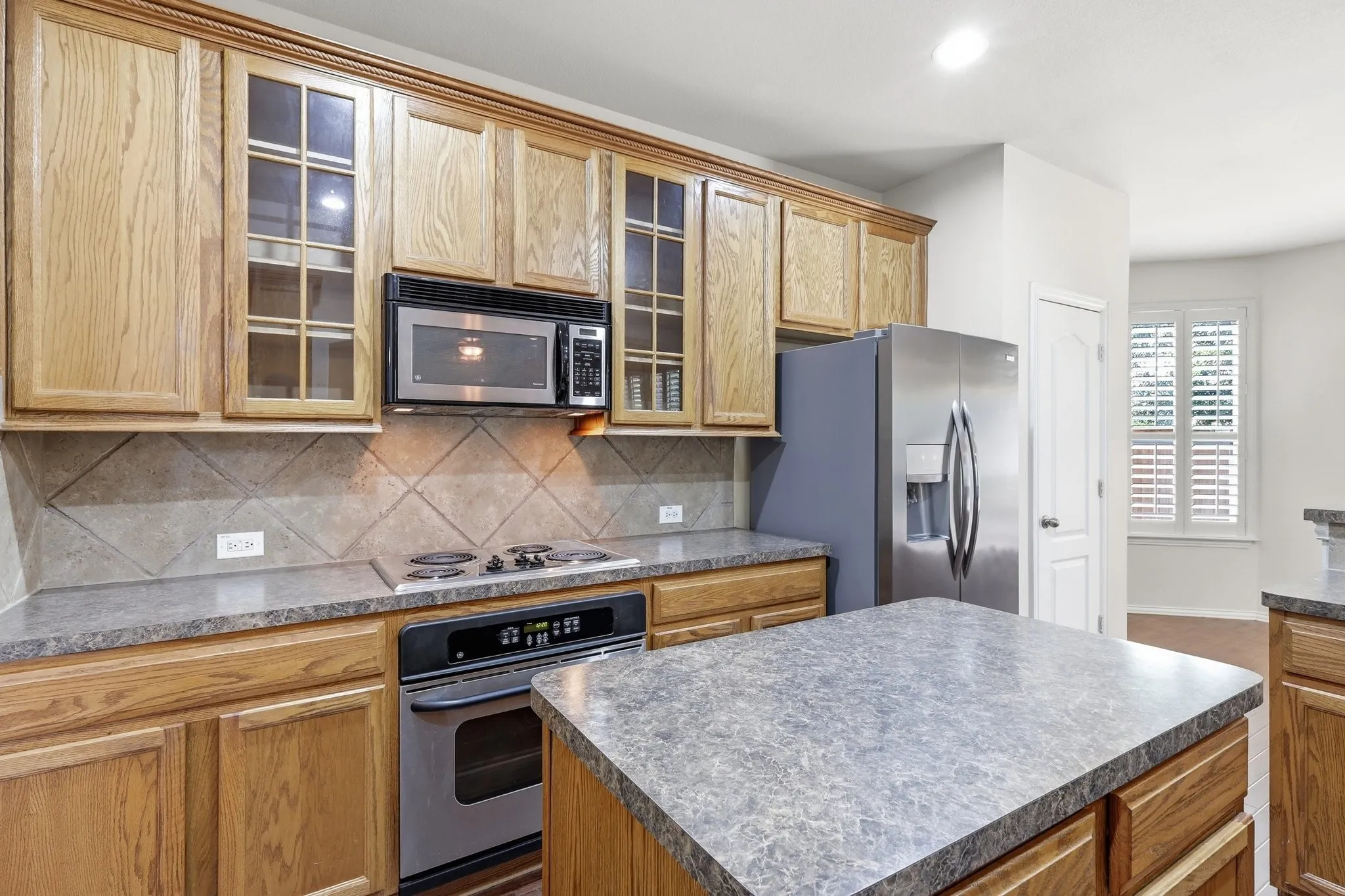 Kitchen featuring wood cabinetry, stainless steel appliances, a built-in microwave, a tile backsplash, and a center island with a stone-finish countertop
