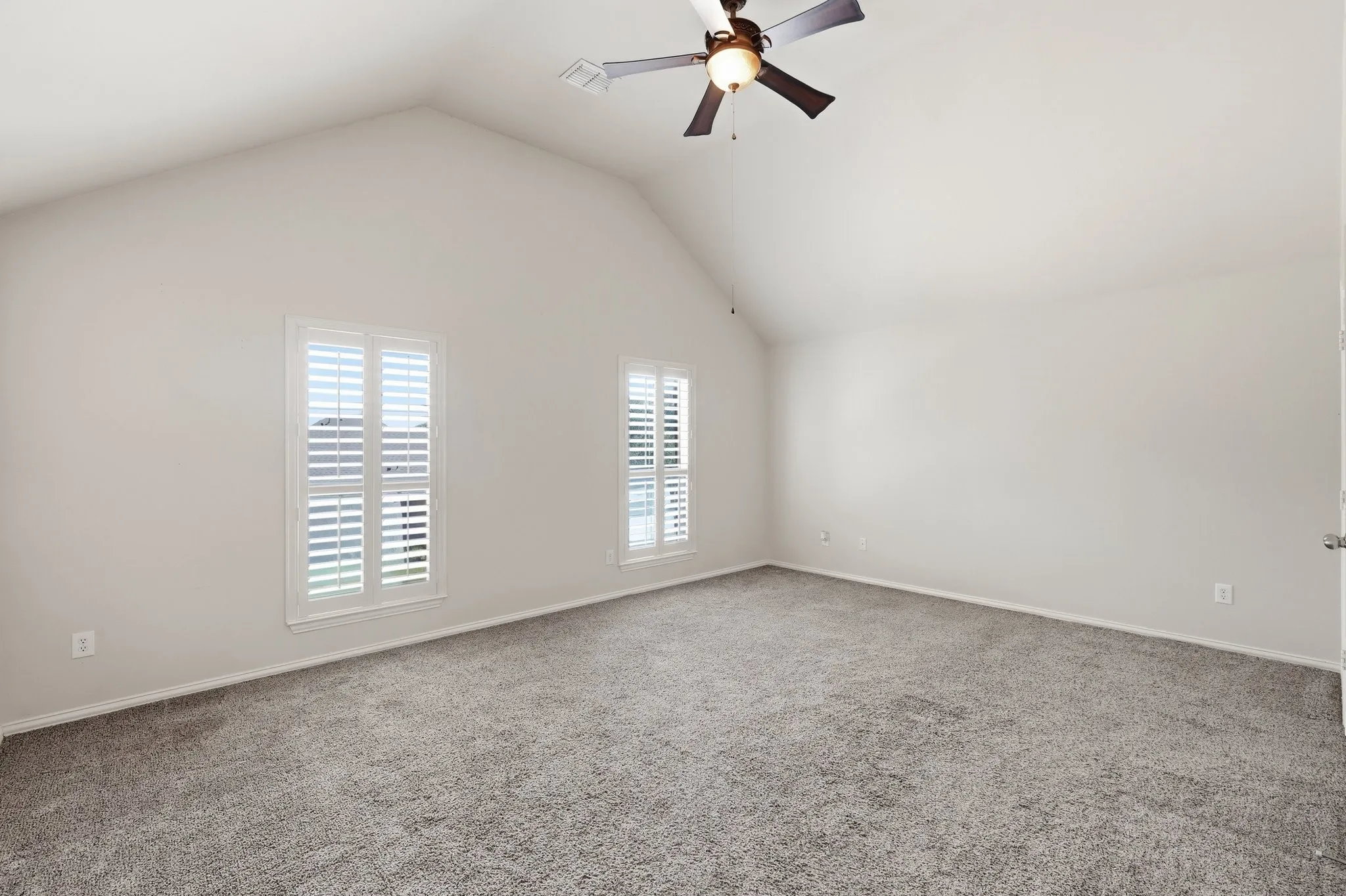 Vaulted ceiling, two windows with plantation shutters, ceiling fan with light fixture, and plush carpeting