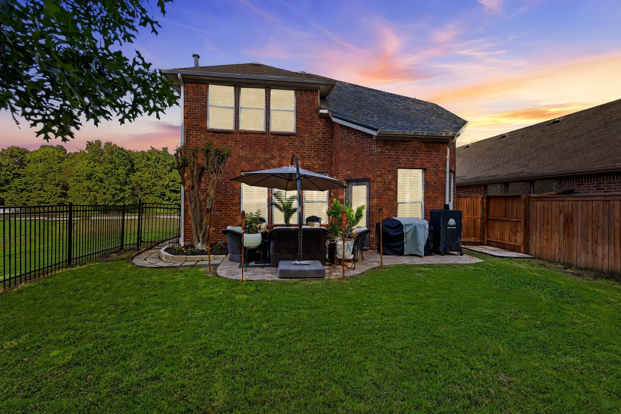 Brick exterior with a stone patio, expansive green lawn, and black metal fencing