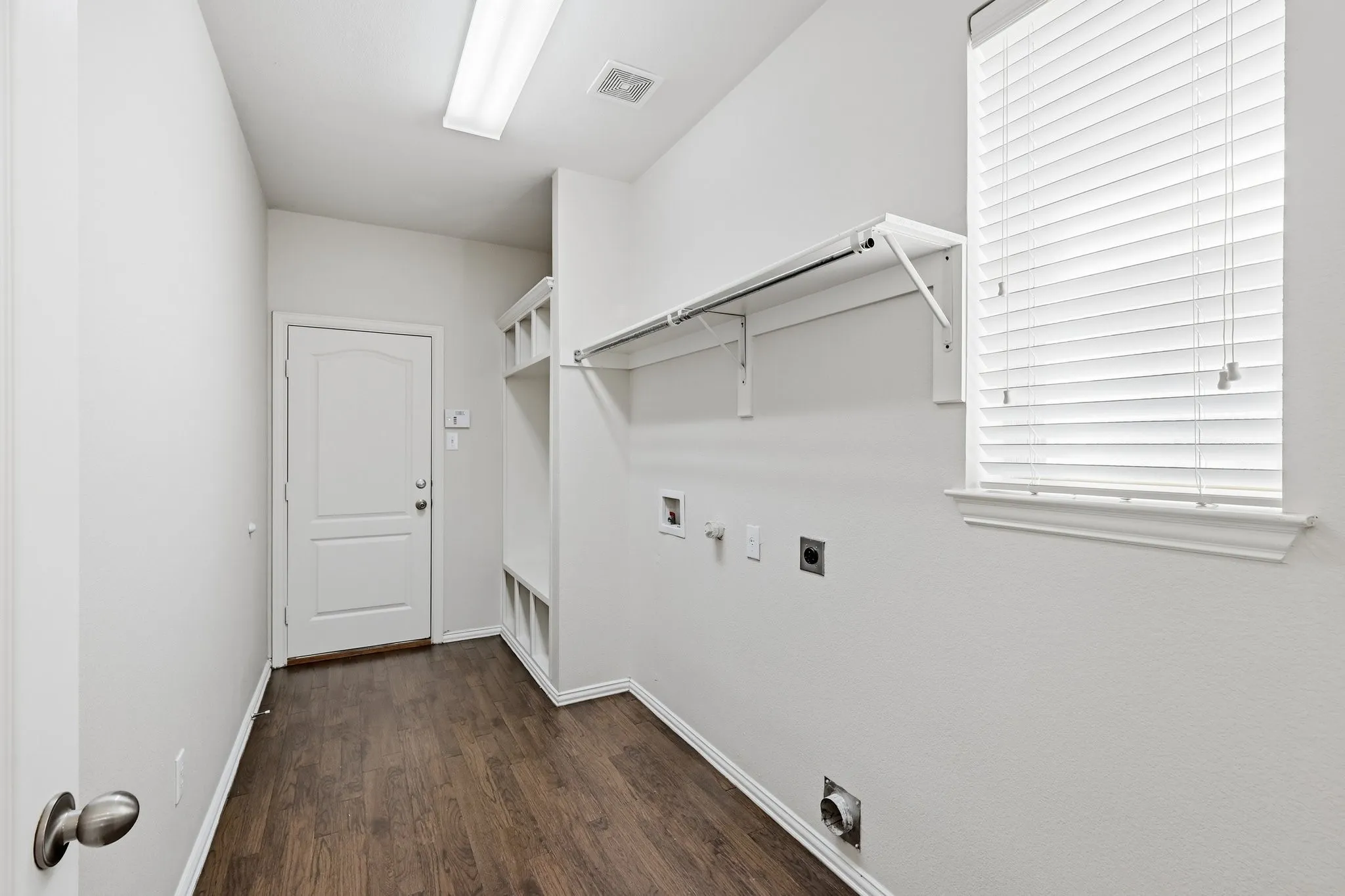 Laundry area featuring wood-finish flooring, built-in shelving, a window with blinds, and overhead lighting