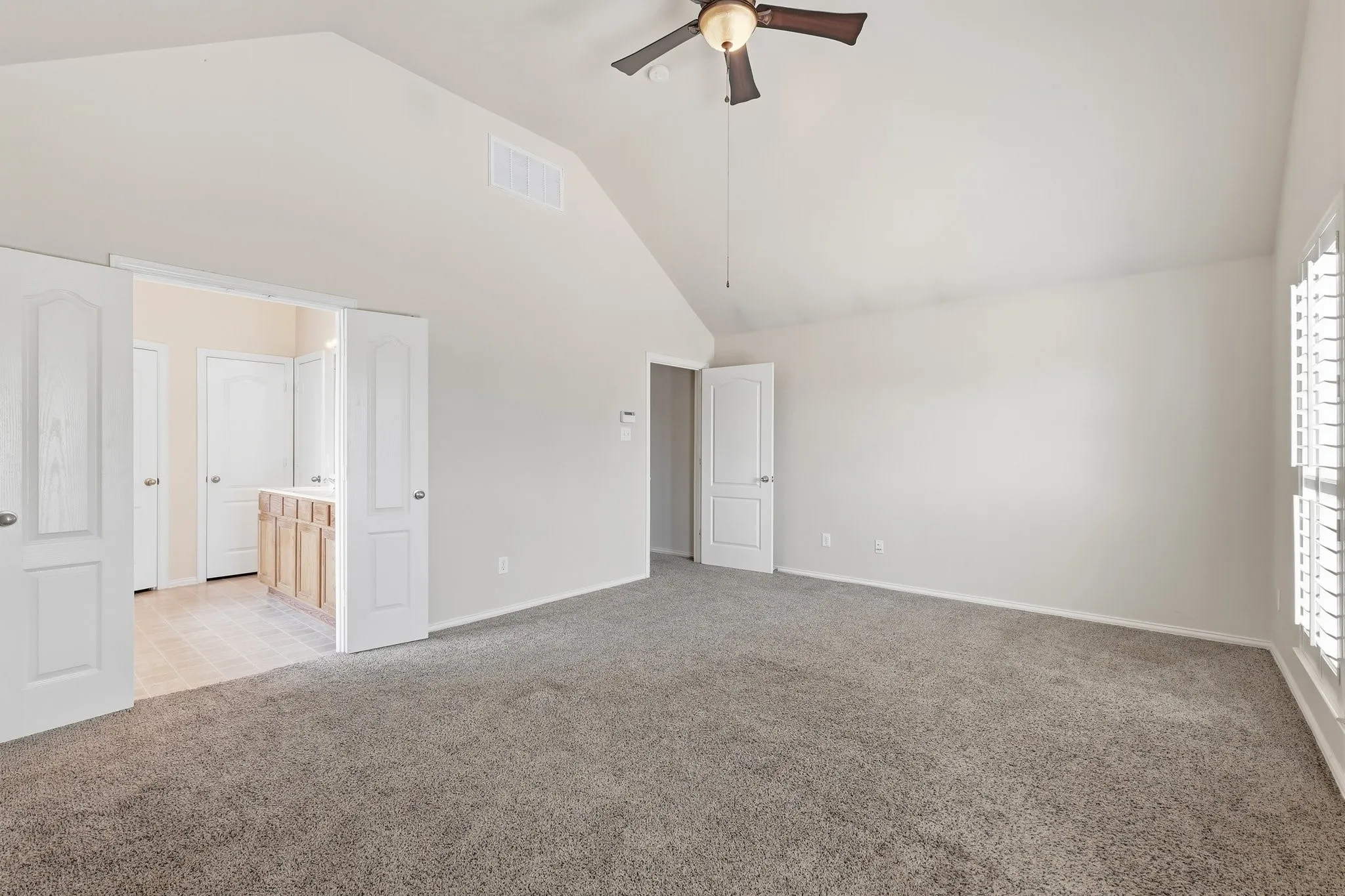 Vaulted ceiling with an integrated ceiling fan, gray carpet flooring, and white plantation shutters