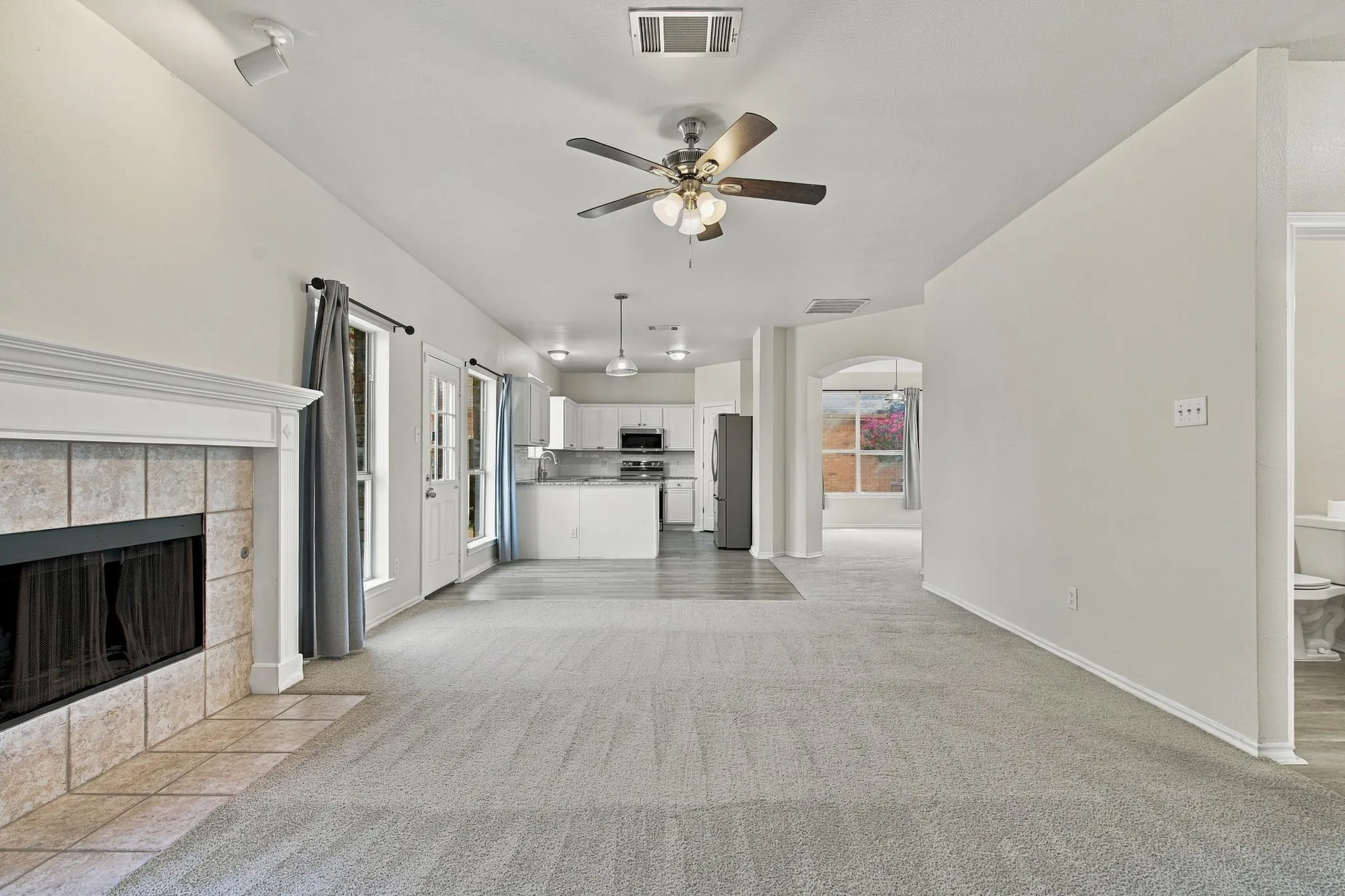 Vaulted ceilings, tile-surround fireplace with mantel, white kitchen cabinetry, recessed lighting, and wood-finish flooring in kitchen