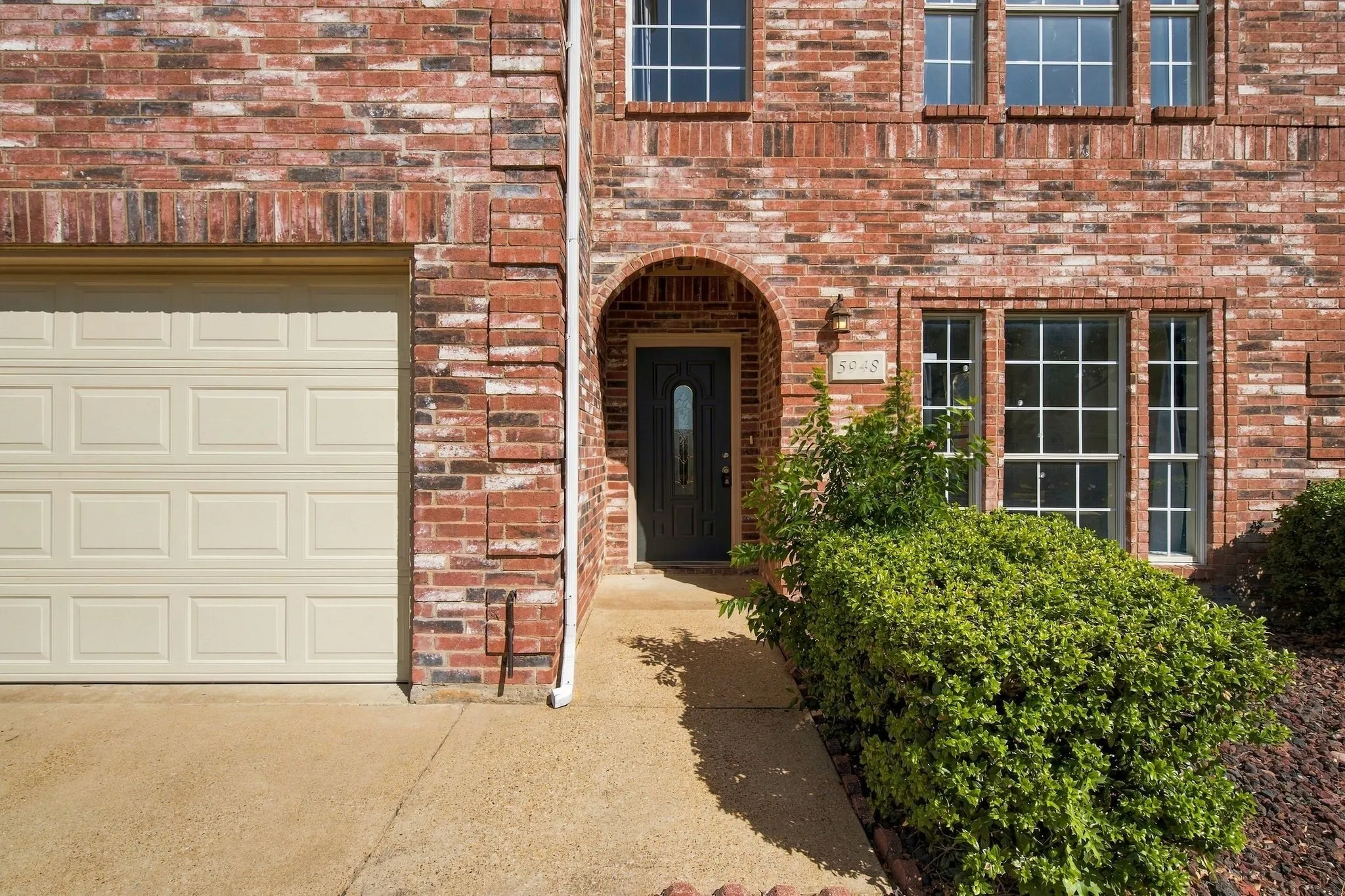 Brick exterior featuring multiple windows with grid patterns, an arched entryway, and an attached garage