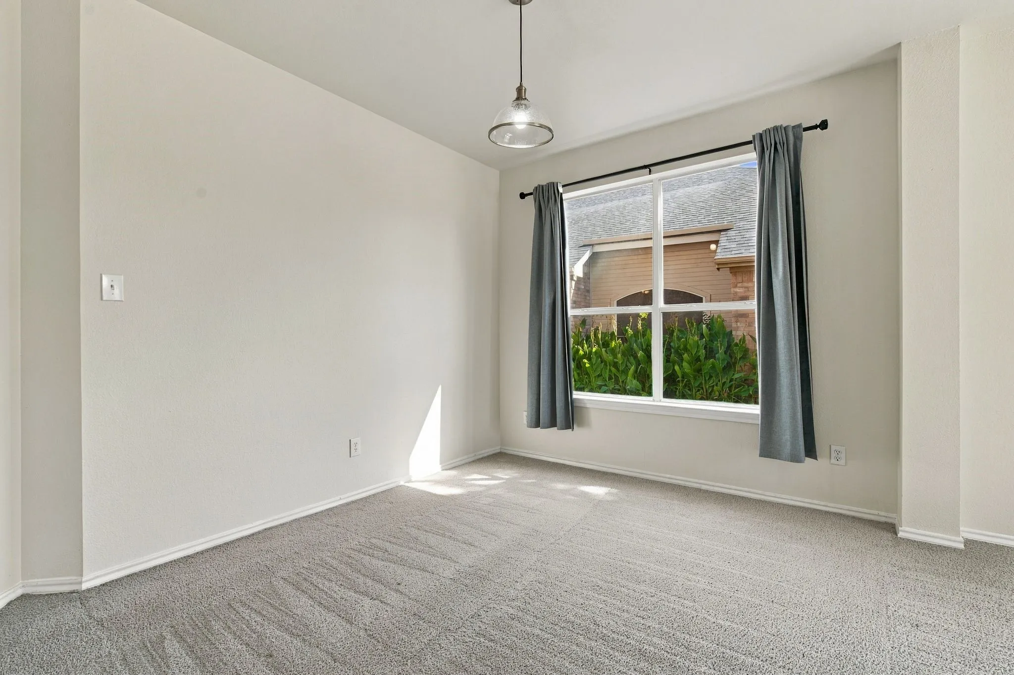 Recessed window with exterior landscaping, light gray carpeting, and a polished pendant light fixture
