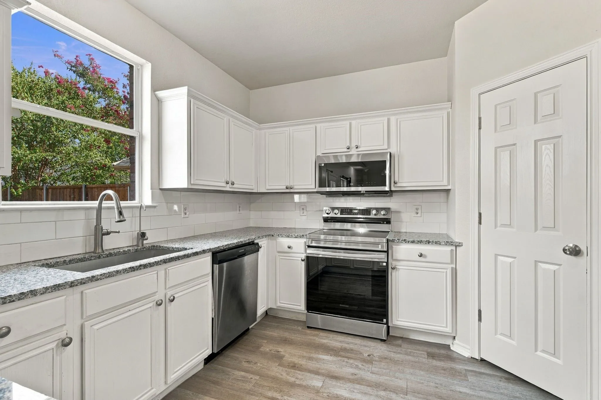 Kitchen with white cabinetry, granite countertops, subway tile backsplash, stainless steel appliances, and wood-finish flooring