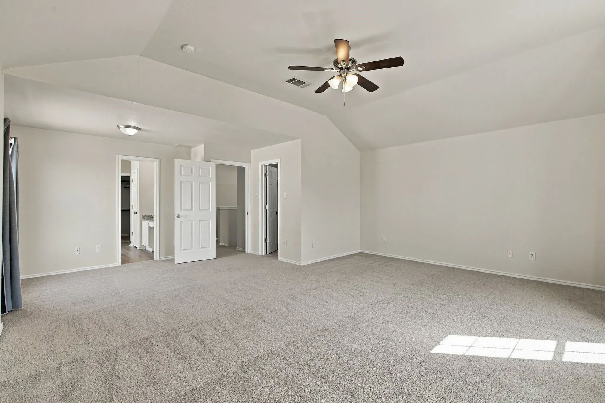 Spacious room featuring vaulted ceilings, light-colored carpeting, a ceiling fan with integrated lighting, and multiple doorways