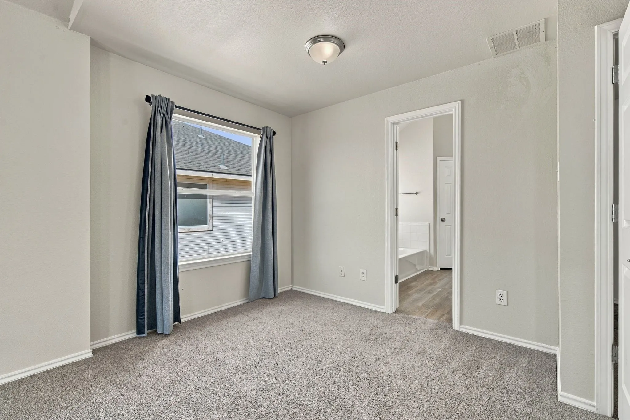 Neutral-toned walls, gray carpeting, and a window with curtain rod