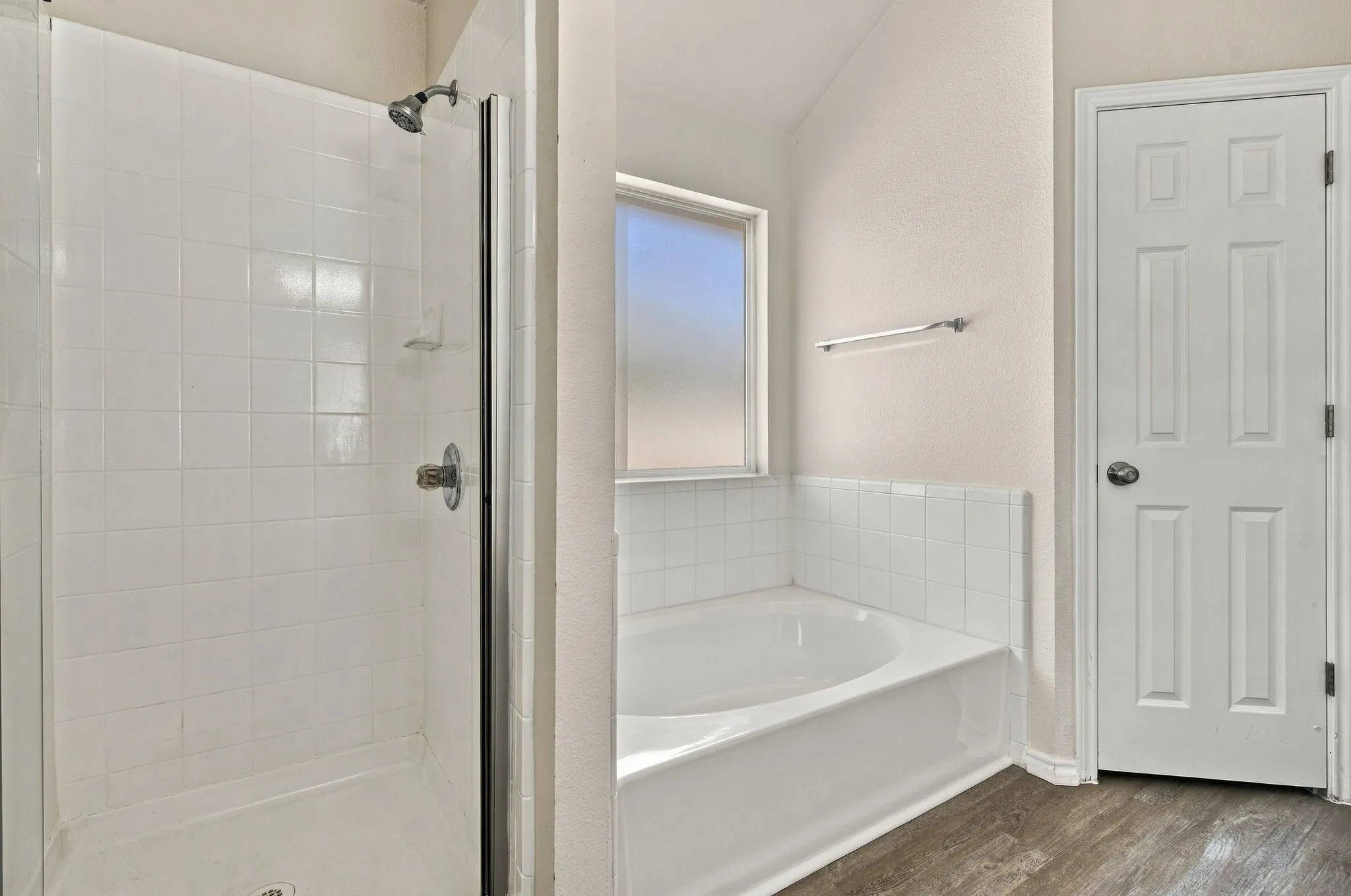 Shower enclosure with glass door, separate built-in soaking tub, frosted window, and wood-finish flooring