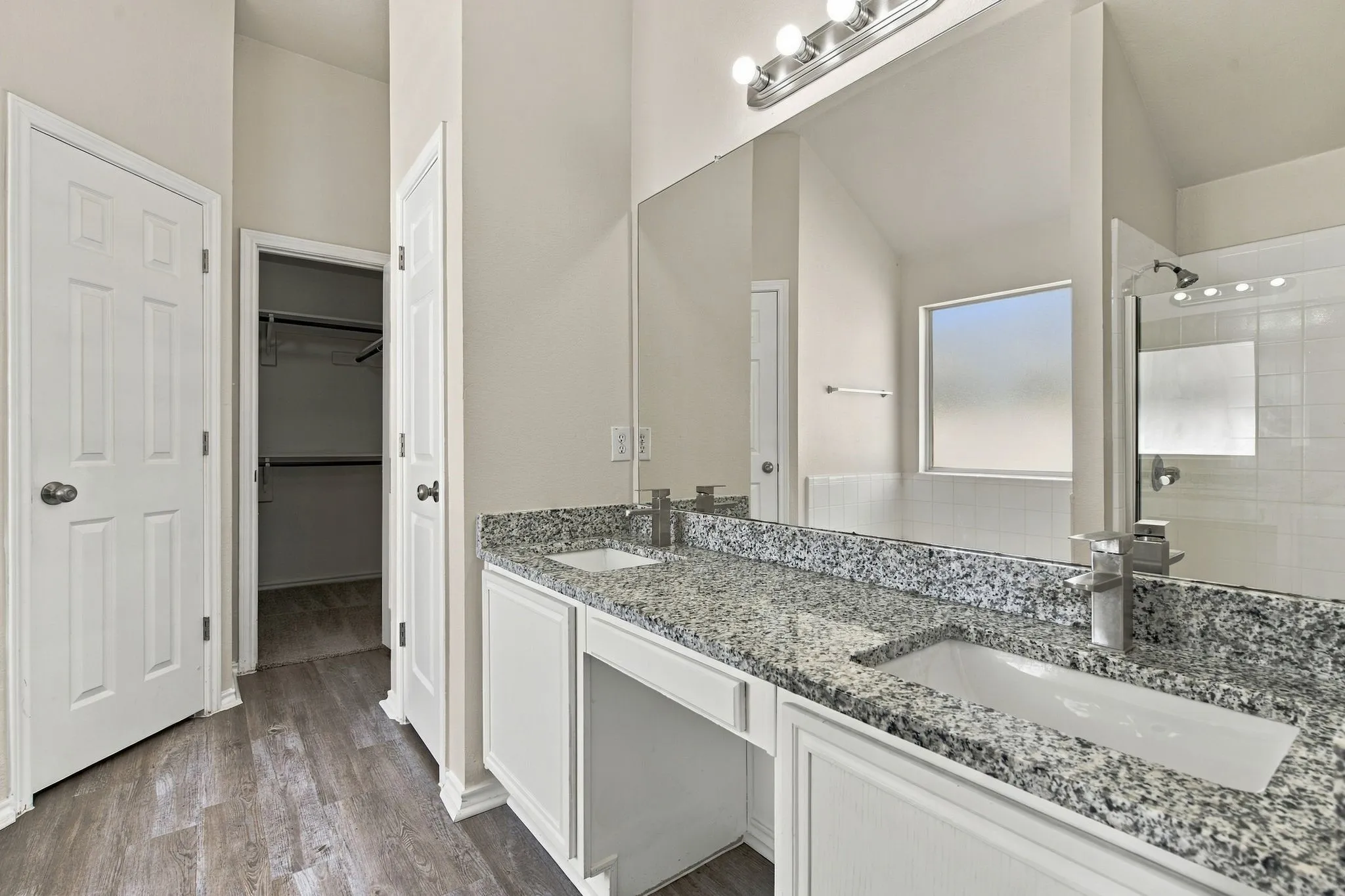 Dual vanity with granite countertops, integrated sinks, white cabinetry, and wood-finish flooring