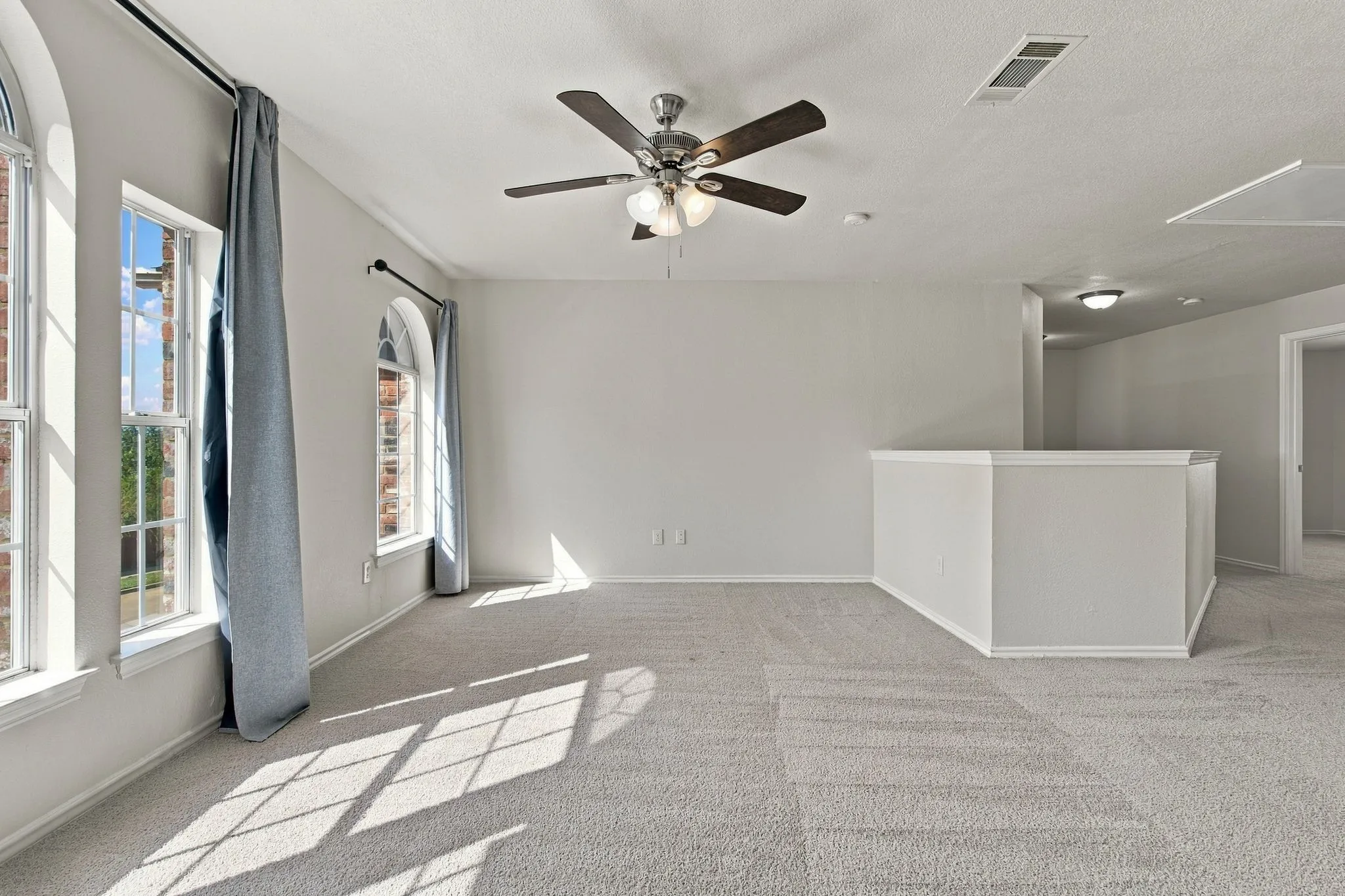 Expansive carpeted area featuring arched windows, a ceiling fan, and a painted half-wall