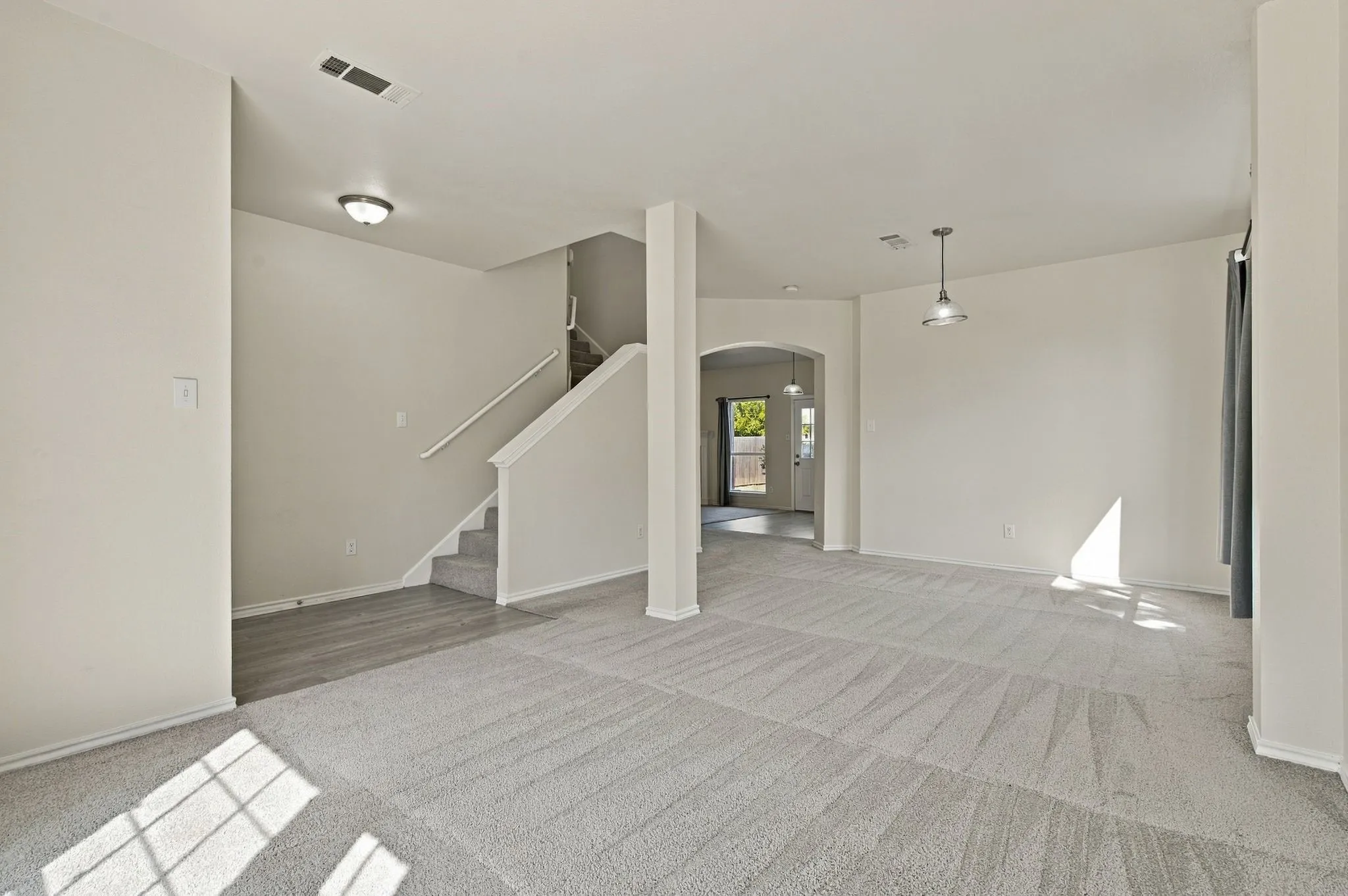 Expansive room featuring light gray carpet, a staircase with gray carpeted treads and white railings, wood-finish flooring, and an arched doorway