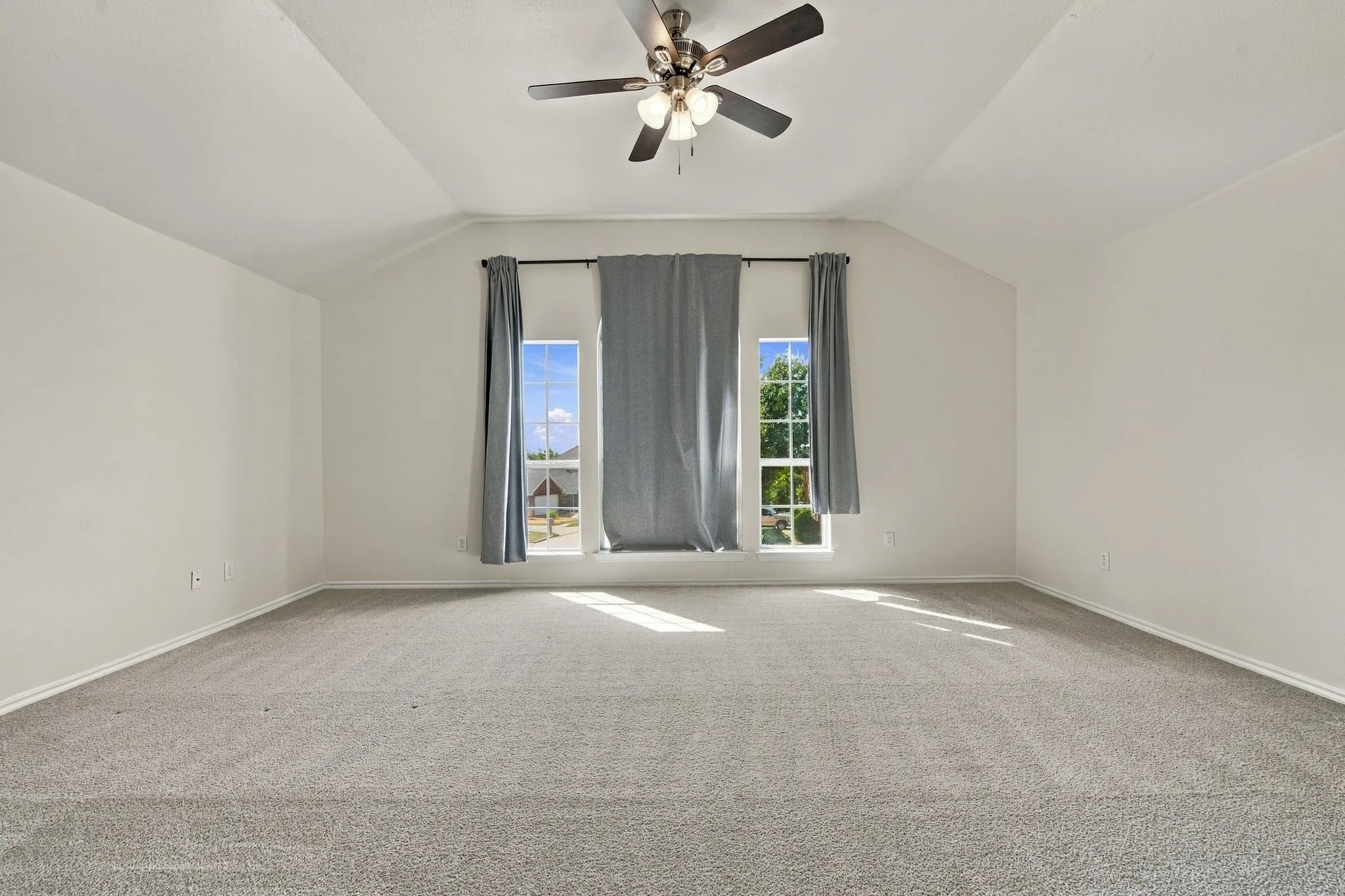 Tray ceiling with a ceiling fan, light gray carpeting, and multiple windows