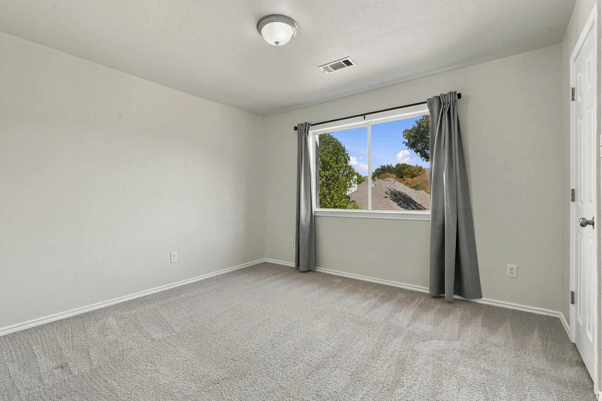 Neutral tone walls, ceiling-mounted light fixture, carpeted flooring, window with exterior scenery, and a paneled interior door