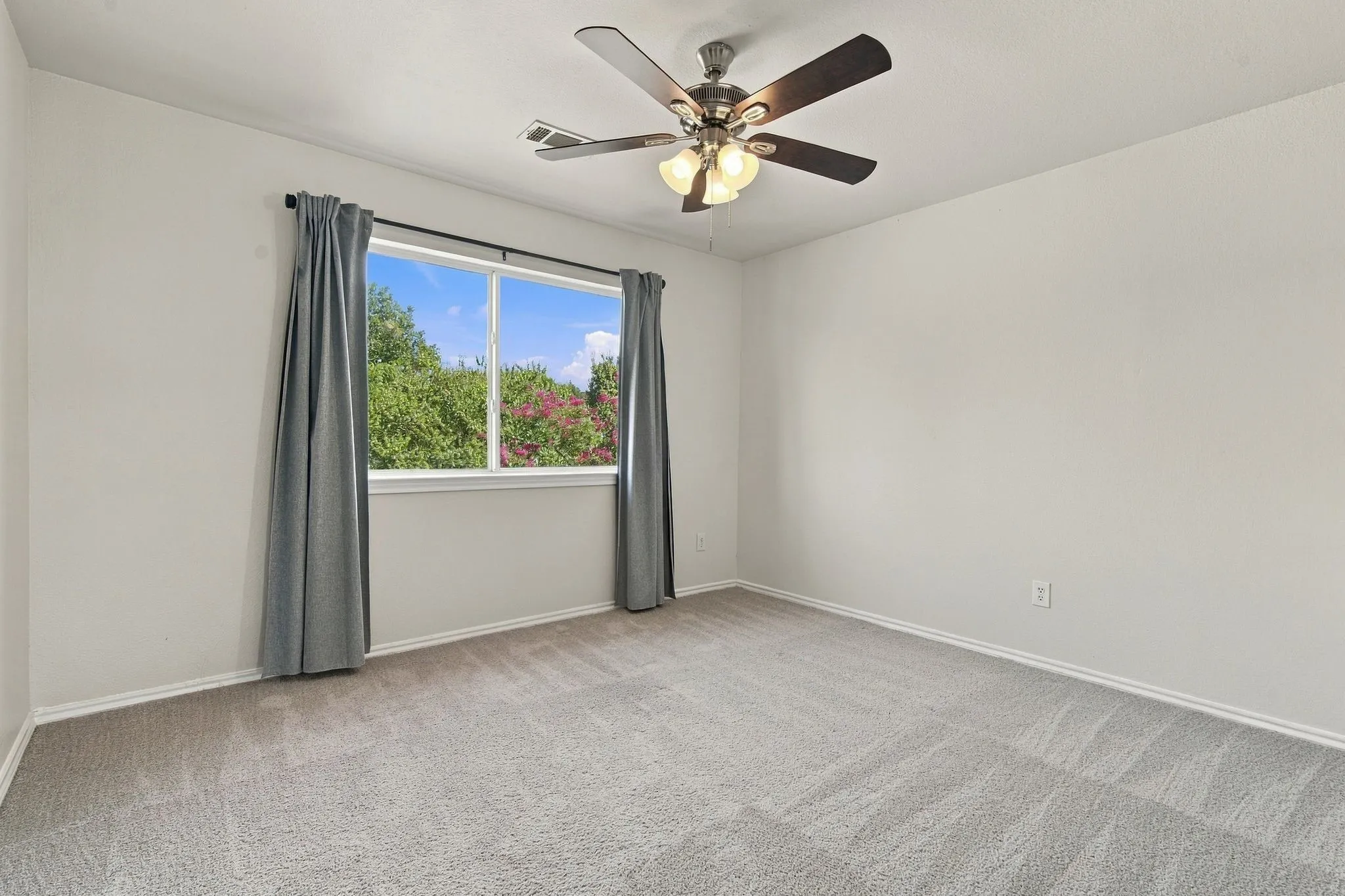 Neutral wall color, carpeted flooring, window with natural scenery, and a ceiling fan with integrated lighting