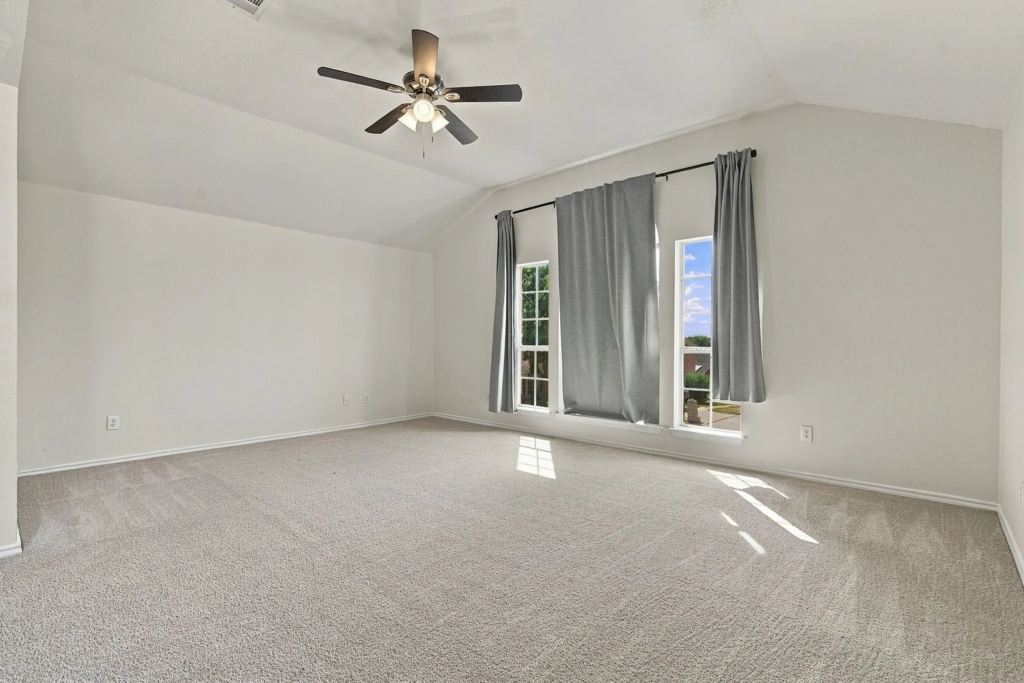 Vaulted ceiling, ceiling fan with integrated lighting, two windows, wall-to-wall carpeting, and neutral wall tones