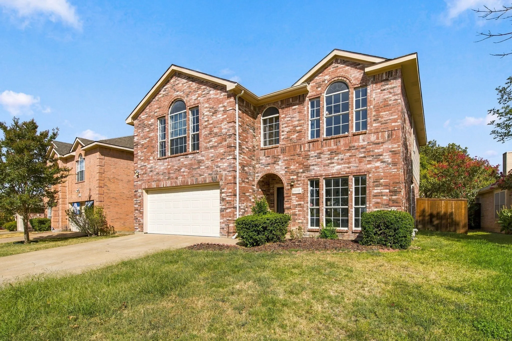 Brick exterior with arched windows, attached garage, and landscaped front yard