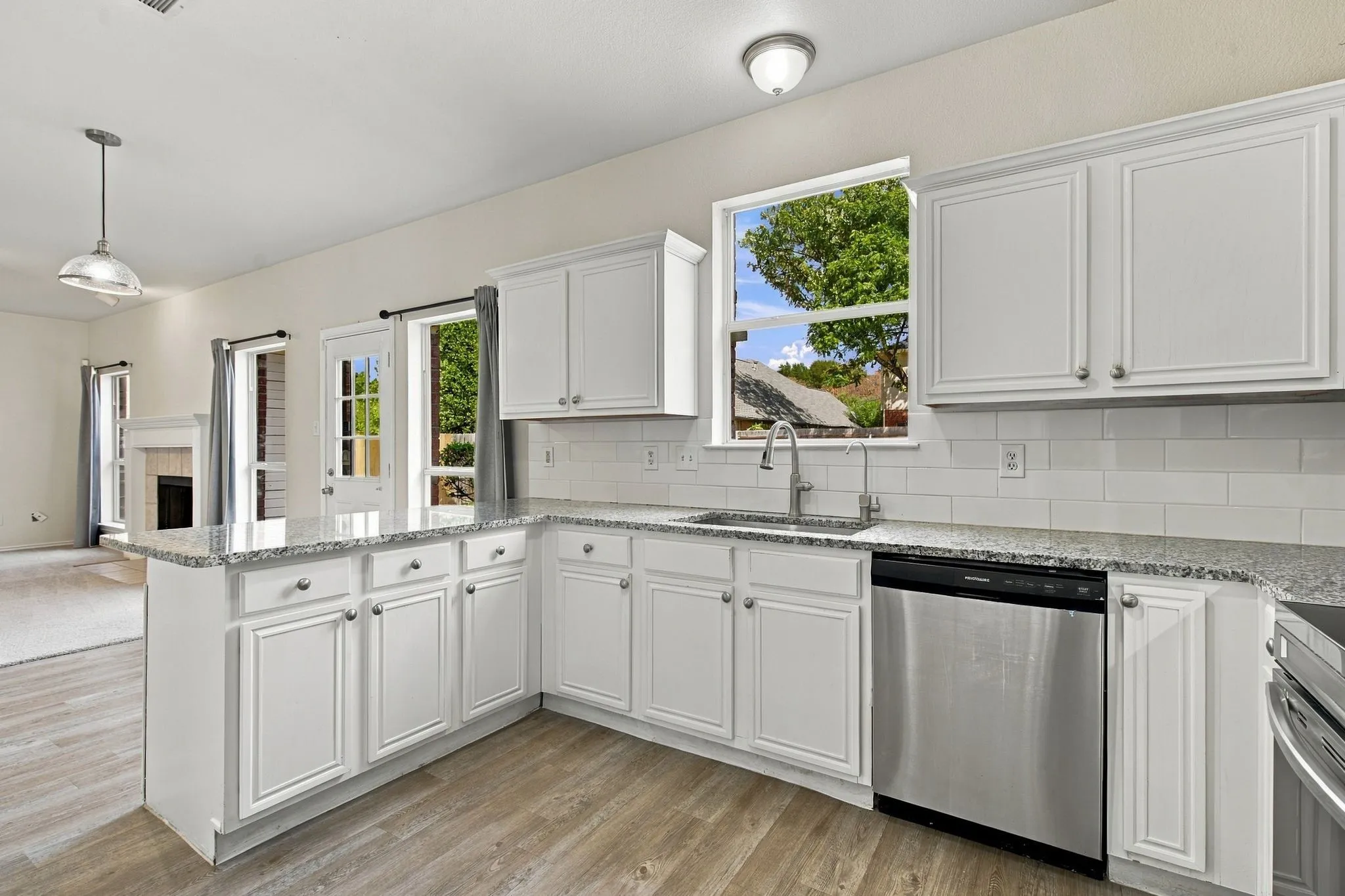 Kitchen featuring white cabinetry, light-toned countertops, a stainless steel dishwasher, and wood-finish flooring