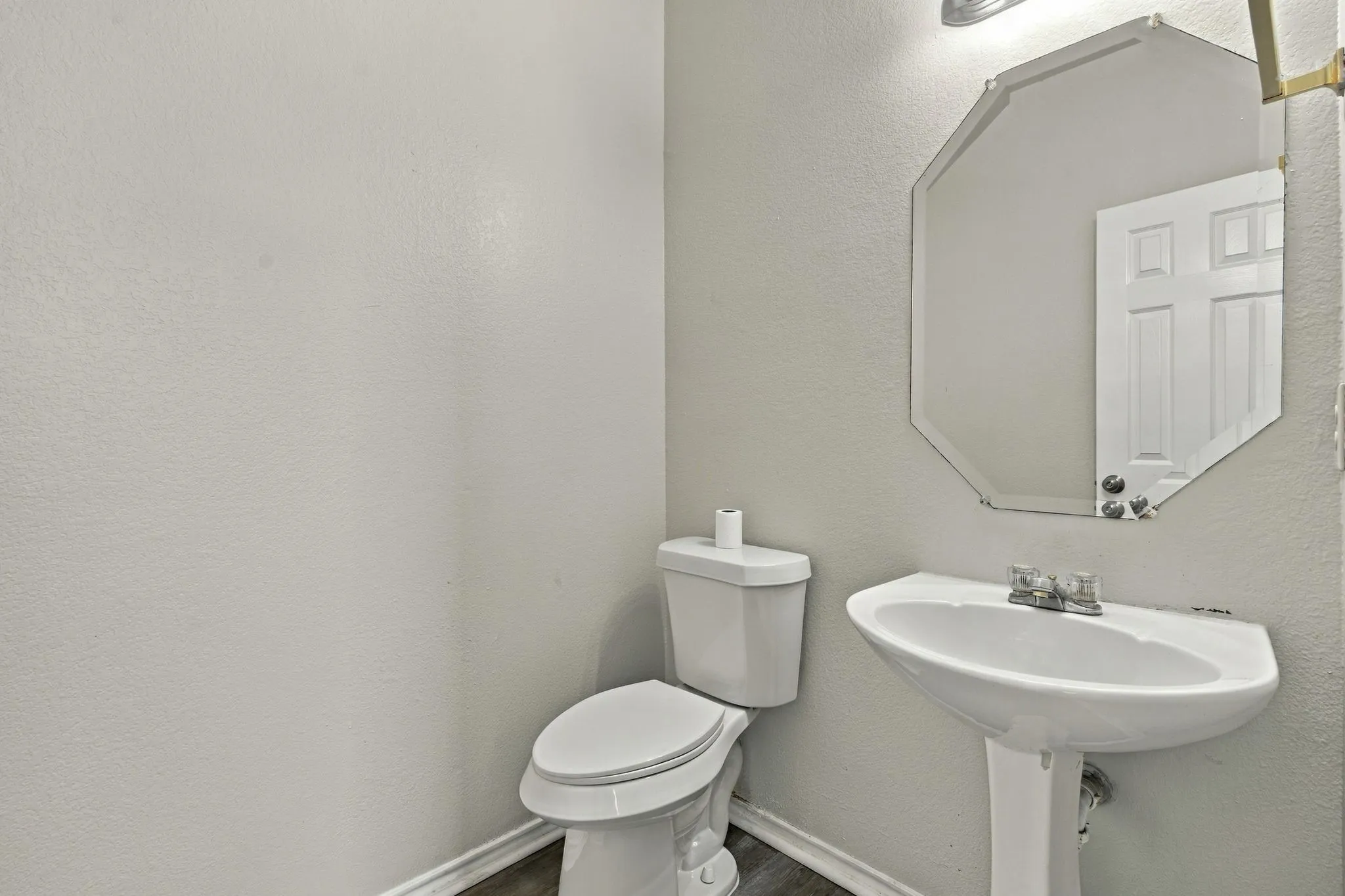 White pedestal sink, modern octagonal mirror, and a two-piece toilet