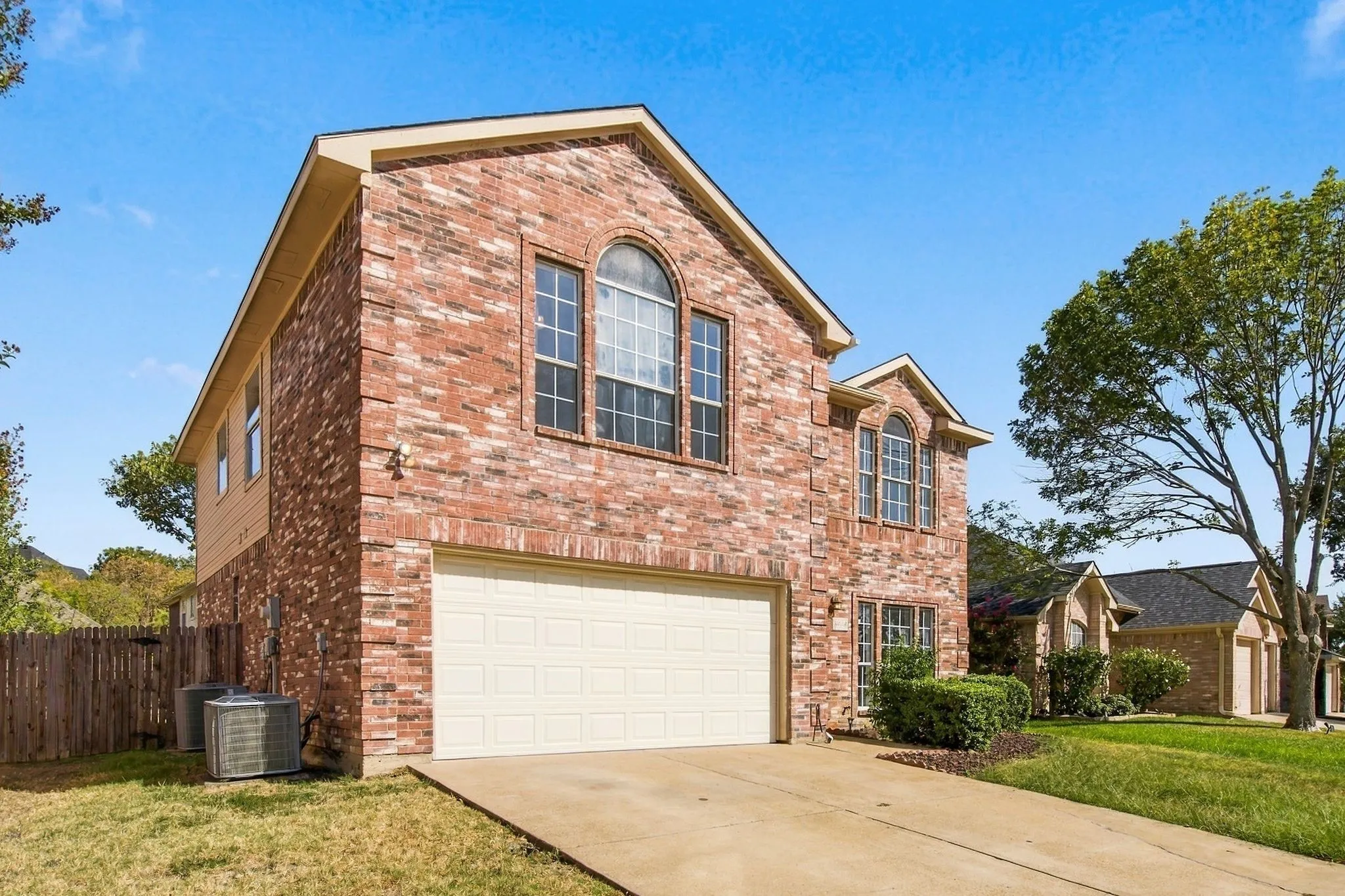 Red brick exterior with arched windows, an attached two-car garage, and a concrete driveway