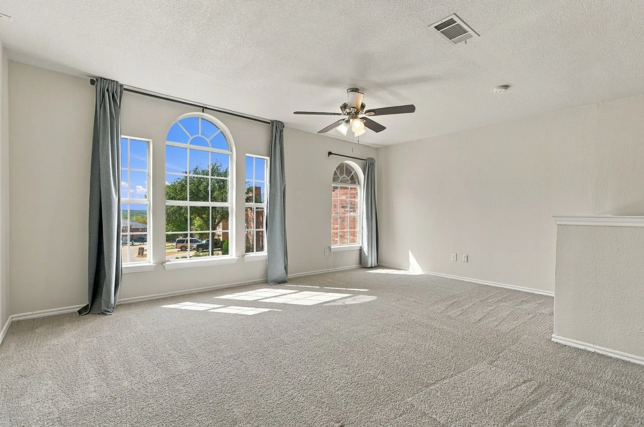 Expansive room with arched windows, light-toned carpeting, and a ceiling fan