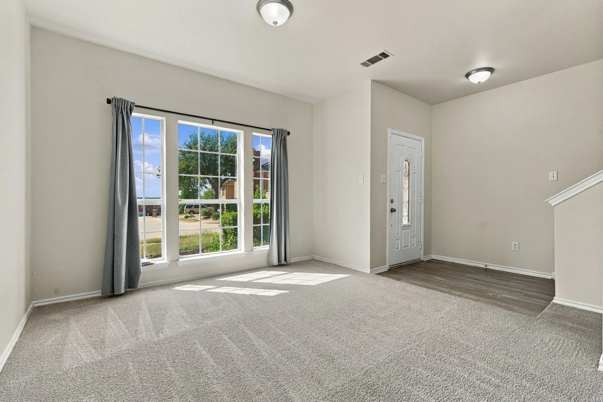 Grey patterned carpeting, light neutral wall paint, white trim, and a white paneled entry door with decorative glass inserts
