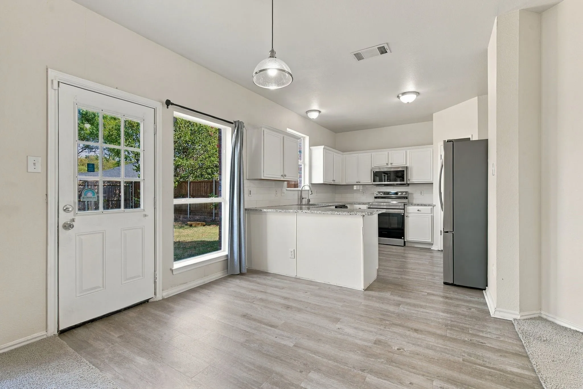 Wood-finish flooring, white cabinetry, stainless steel appliances, and an island with a countertop