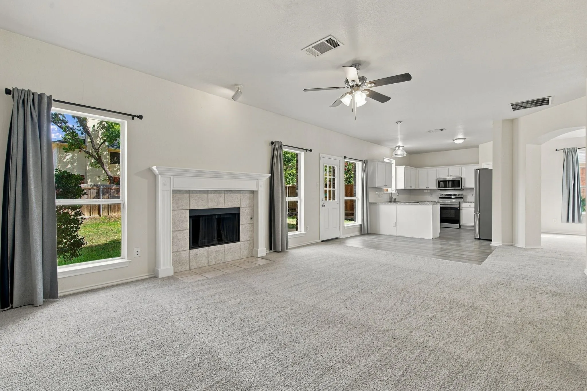 Fireplace with tile surround, light-toned carpeting, white kitchen cabinetry, stainless steel appliances, and wood-finish flooring