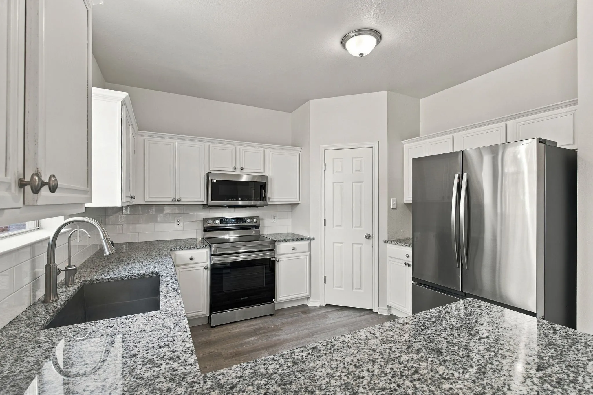 Kitchen featuring granite countertops, white cabinetry, stainless steel appliances, a subway tile backsplash, and wood-finish flooring