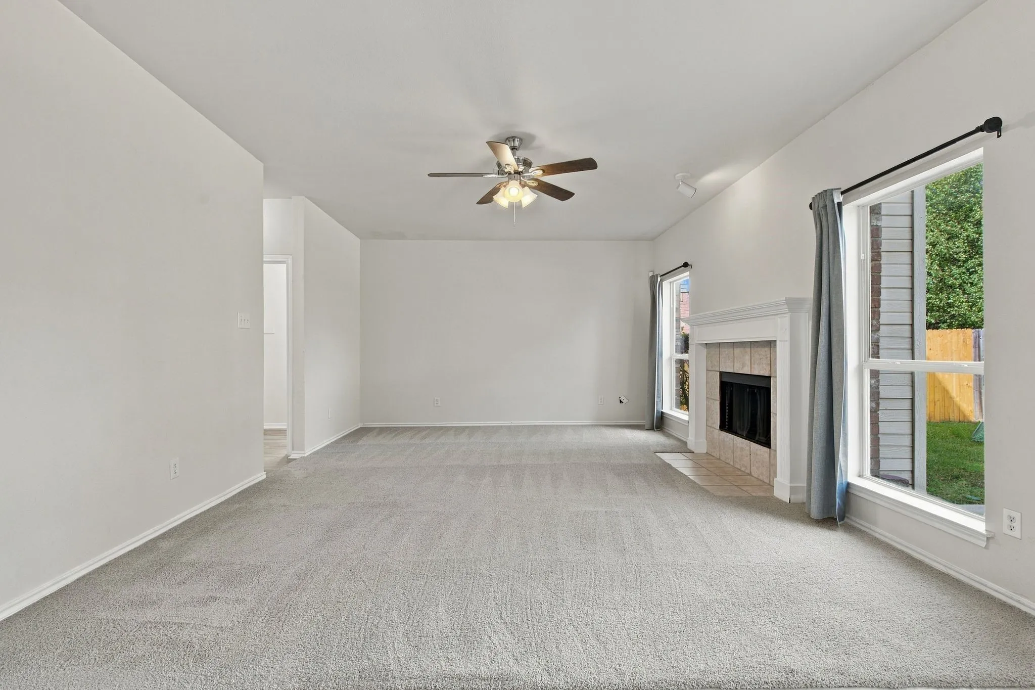 Spacious room featuring light-toned carpeting, a fireplace with a white mantel and tile surround, and multiple windows